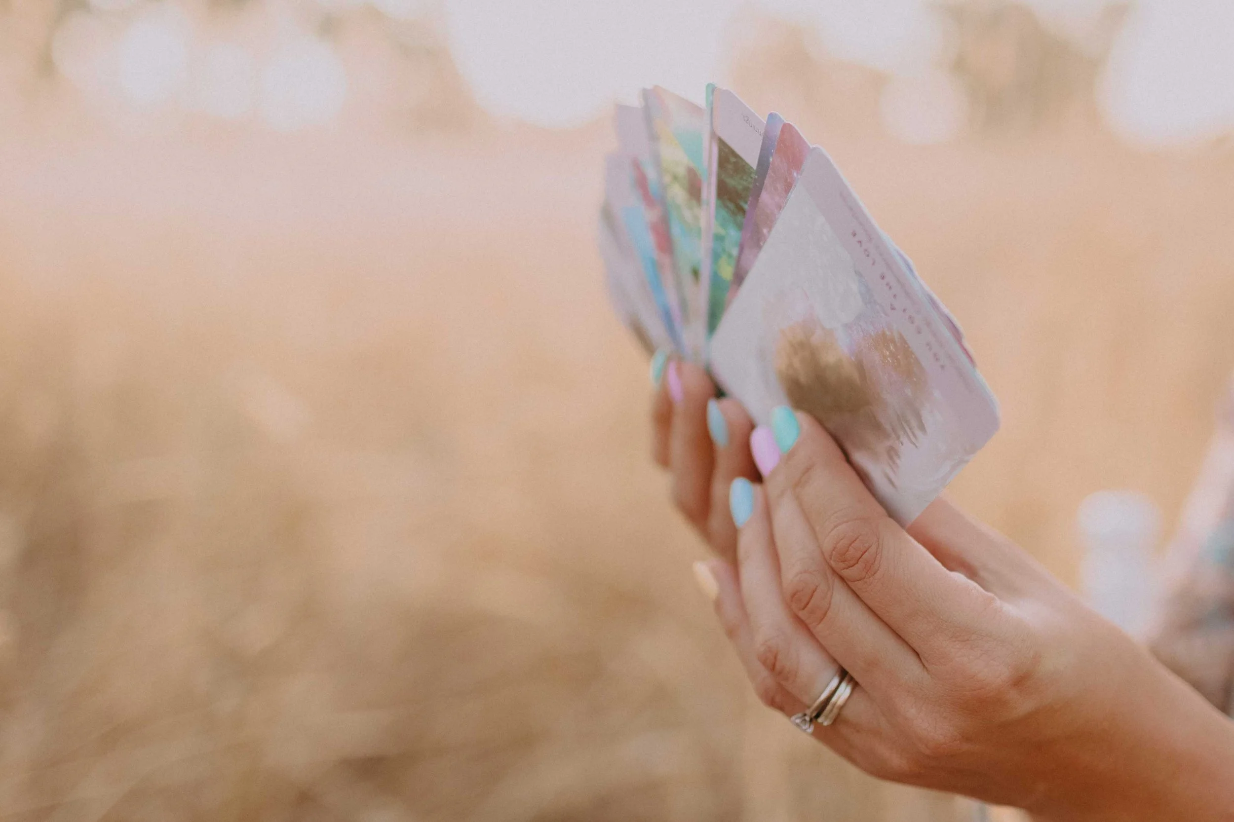 A person with colorful manicured nails holding a small stack of colorful greeting cards or papers against a blurred background.