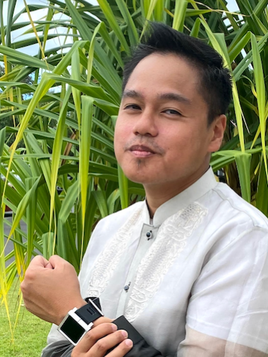 Man in white traditional shirt posing in a lush green field of tall plants.