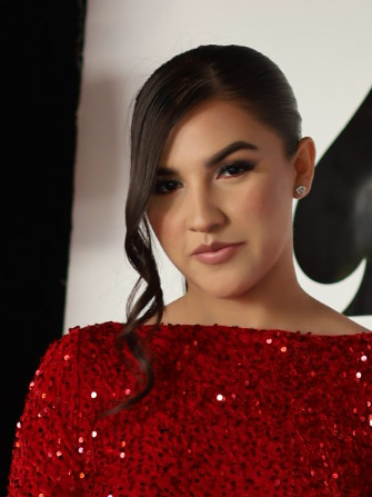 A woman with dark hair styled in loose waves, wearing a red sequined dress, posing indoors.