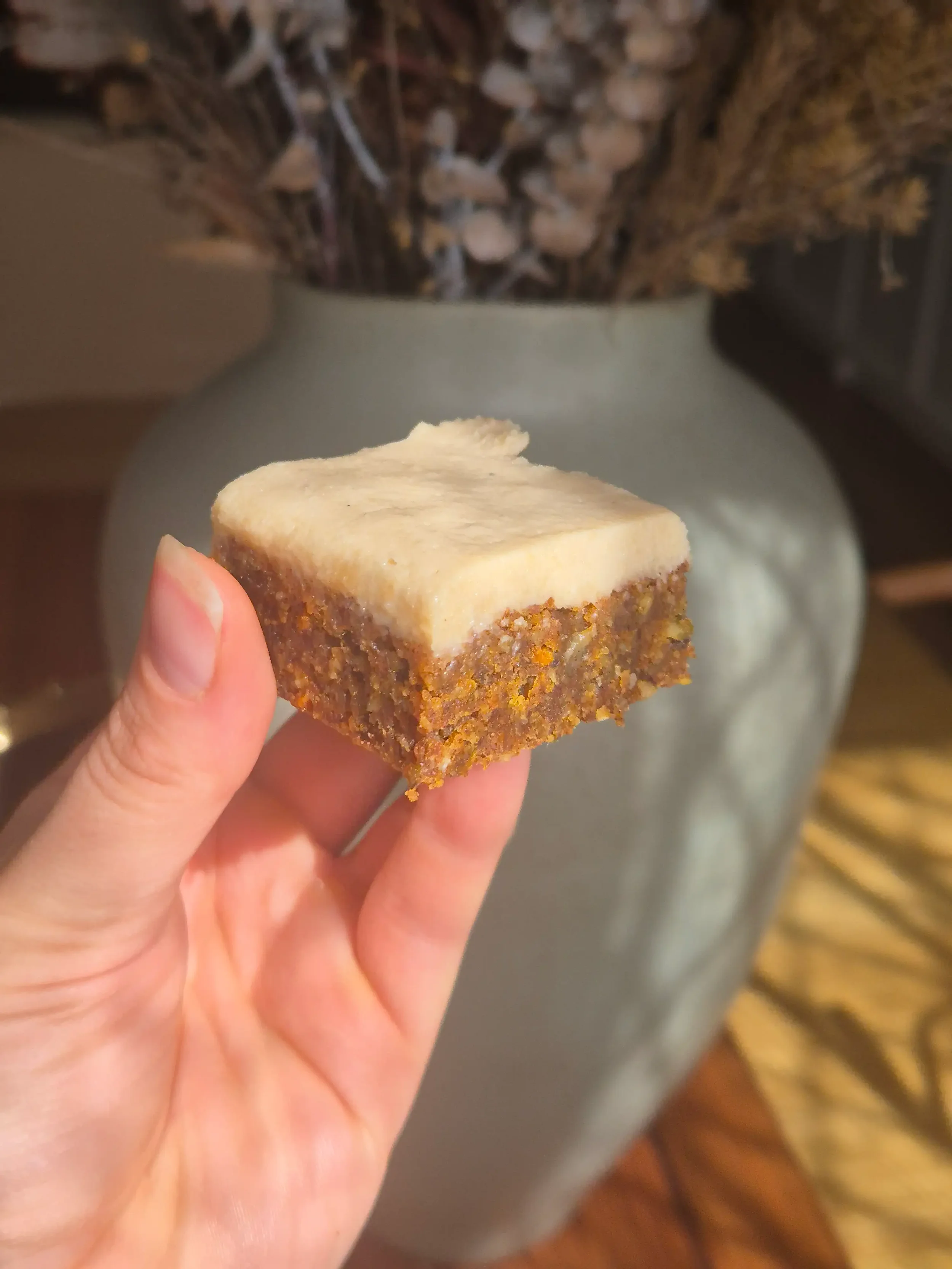 Hand holding a slice of healthy Easter carrot cake protein bar with creamy Greek yoghurt topping