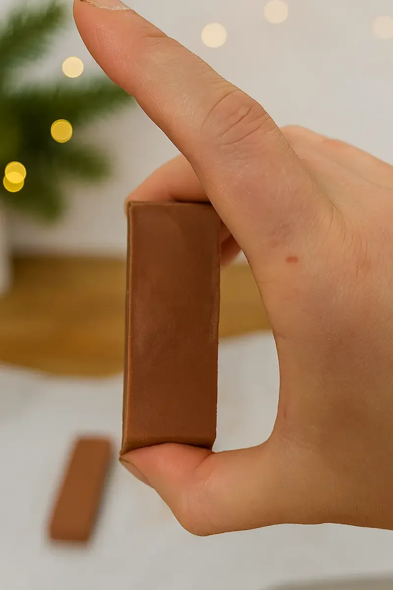 Hand holding up a glossy piece of healthy peanut butter fudge, rich with dark chocolate and perfect for festive homemade gifting.