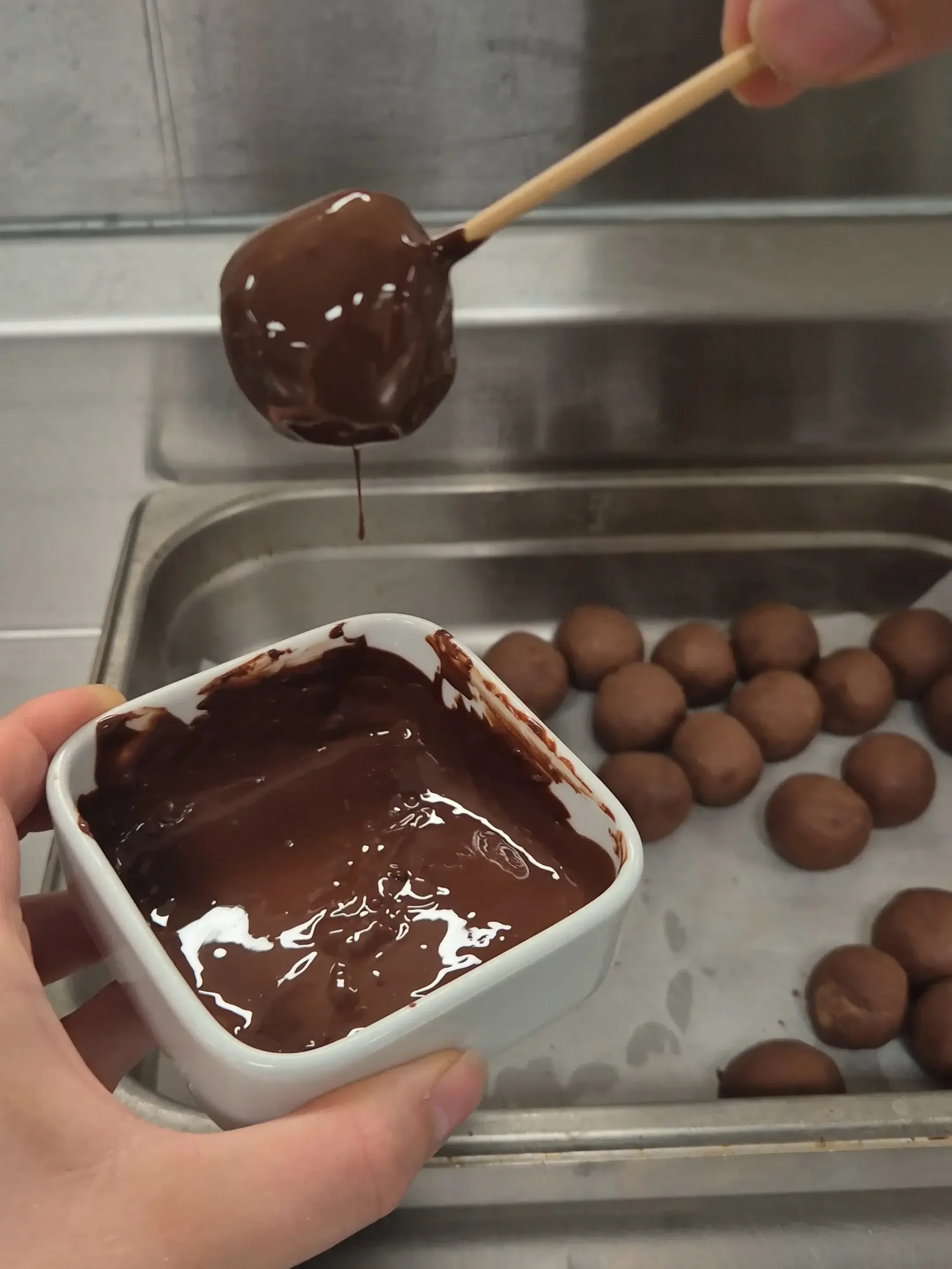 A chocolate chickpea truffle being dipped into melted dark chocolate before setting.