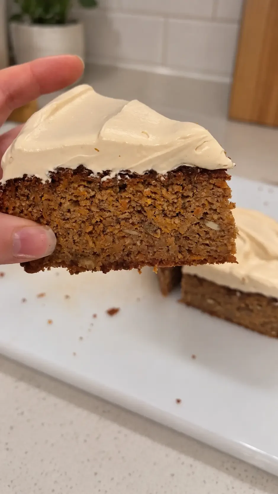 Hand holding a slice of homemade healthy carrot cake made with grated carrots, almond meal and warm cinnamon spices.