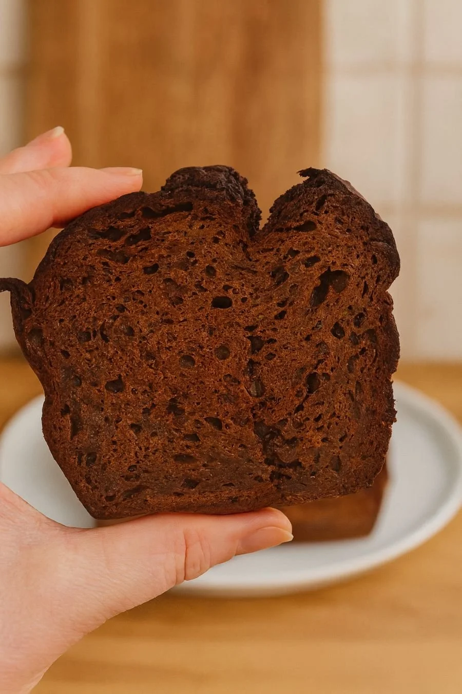 A close-up of a freshly toasted slice of carrot, zucchini and apple bread held up to the camera, showing its golden edges and fluffy crumb.