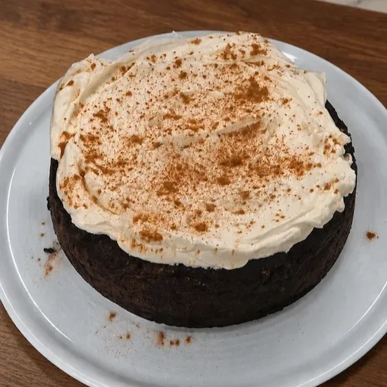 Whole fudgy chocolate tahini sweet potato cake topped with sesame seeds on a serving plate.