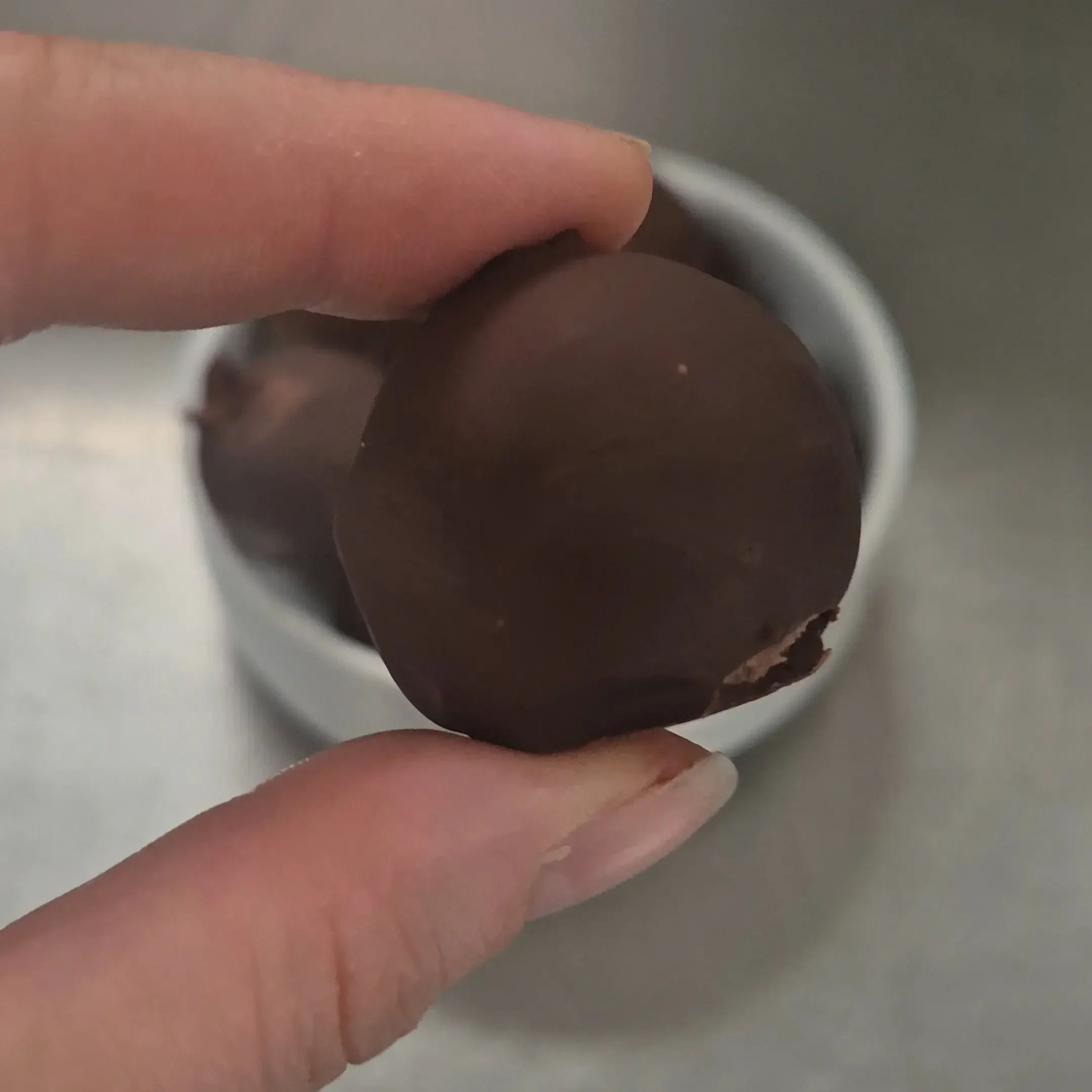 Courtney holding an easy chocolate chickpea truffle in front of the camera, with homemade truffles in the background.