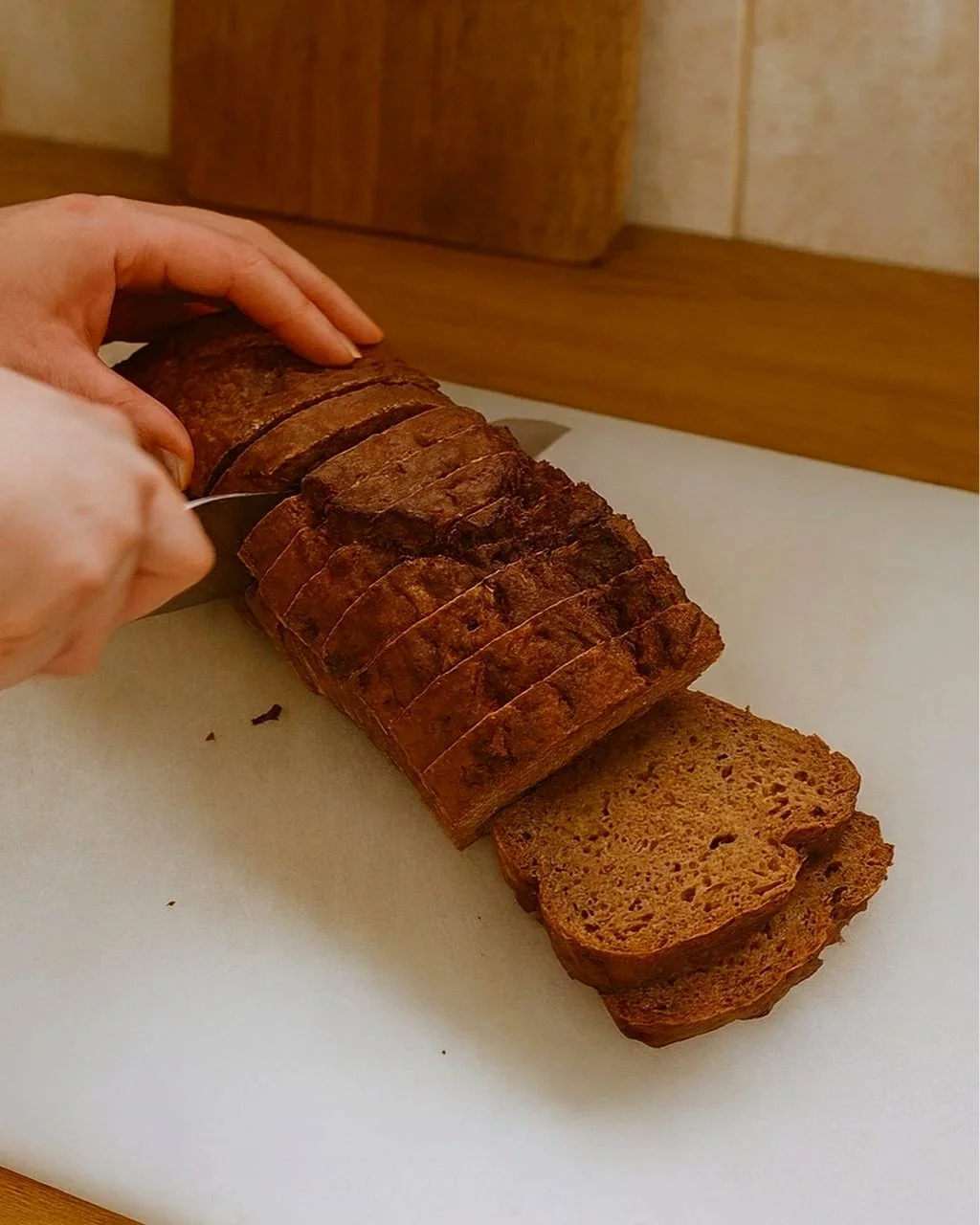 A carrot, zucchini and apple bread loaf being sliced on a board, showing the moist, speckled texture inside with grated apple and vegetables.