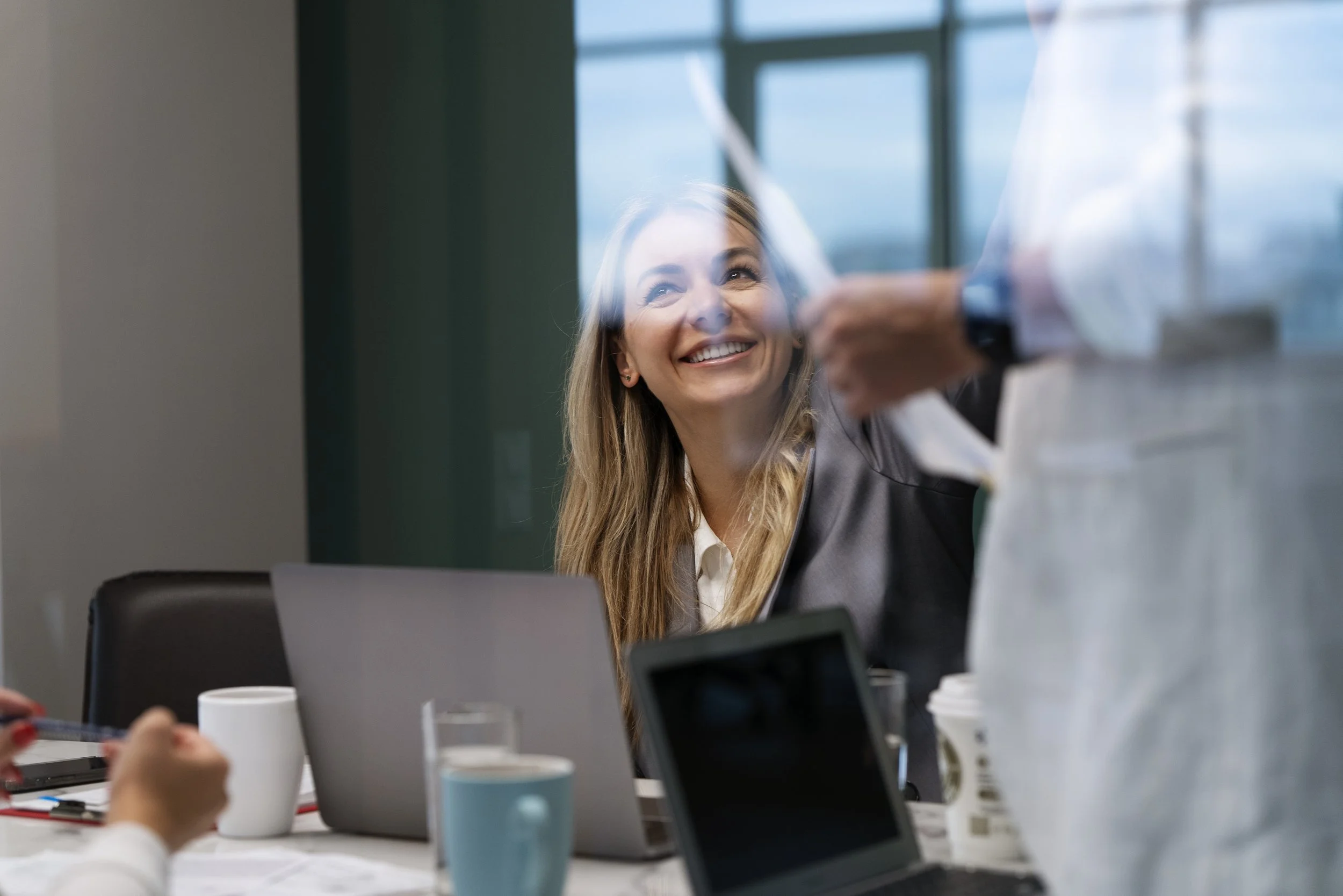 Smiling woman in an office meeting with laptops and coffee cups.