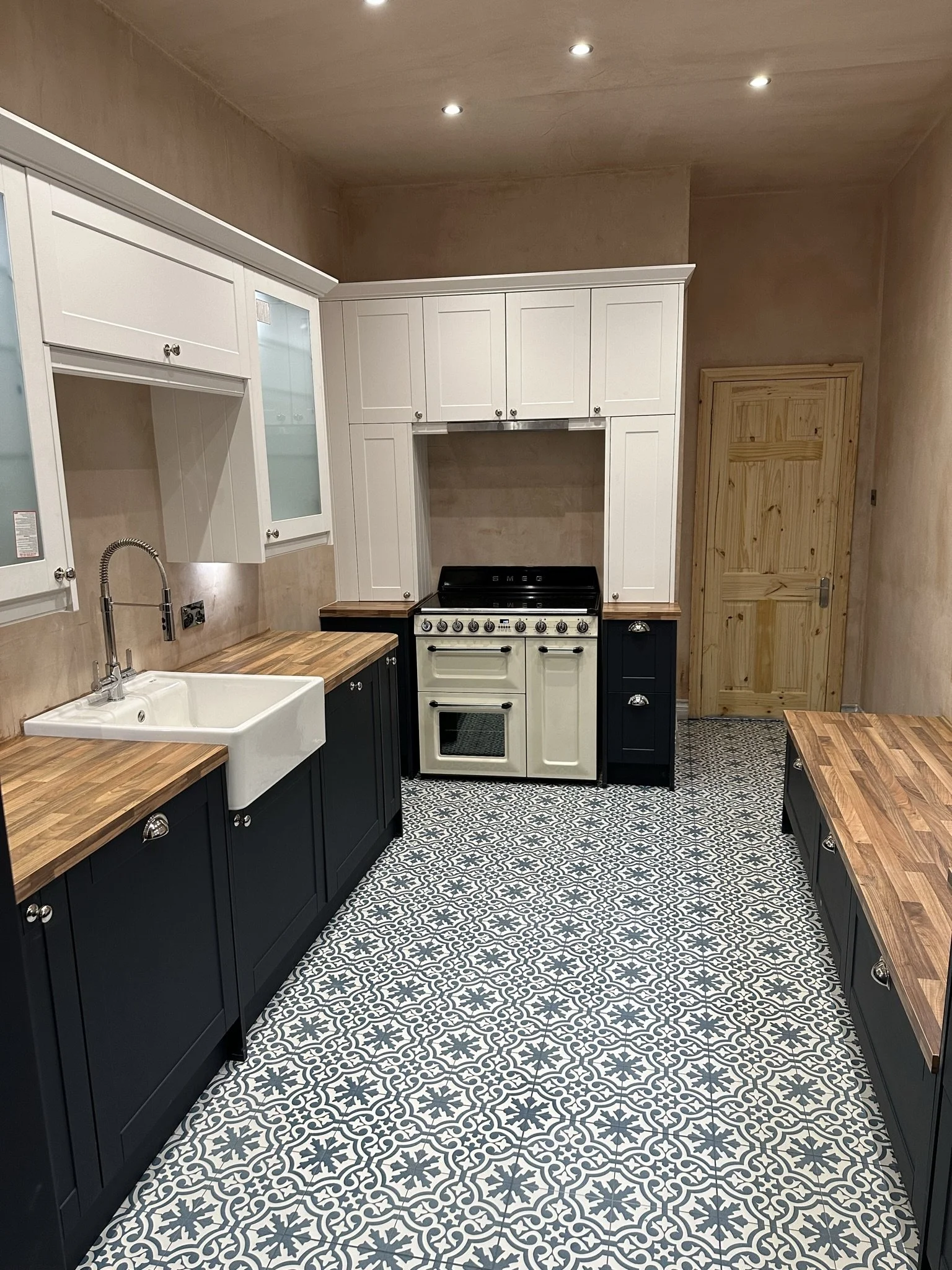 Kitchen in sunderland with black and white cabinetry, wooden countertops, a belfast sink, and patterned tile flooring.