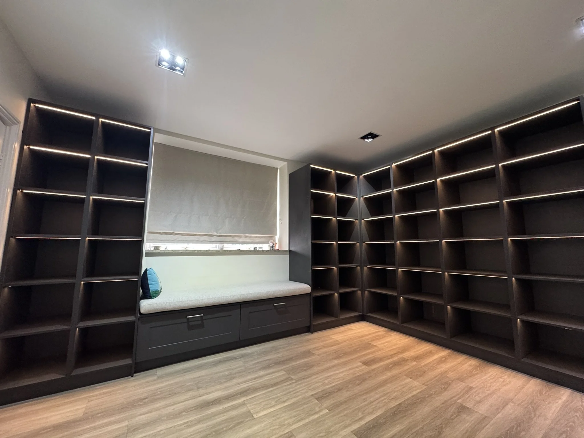 Empty dark wood bookshelves in a room with a built-in window seat and light wood flooring.