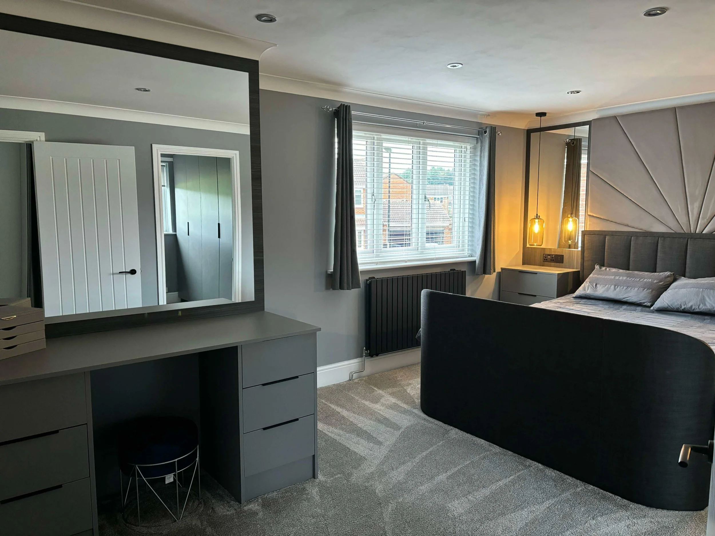A modern bedroom in Washington tyne and wear with a large bed, nightstands, pendant lighting, window with blinds, and a dresser with mirror.