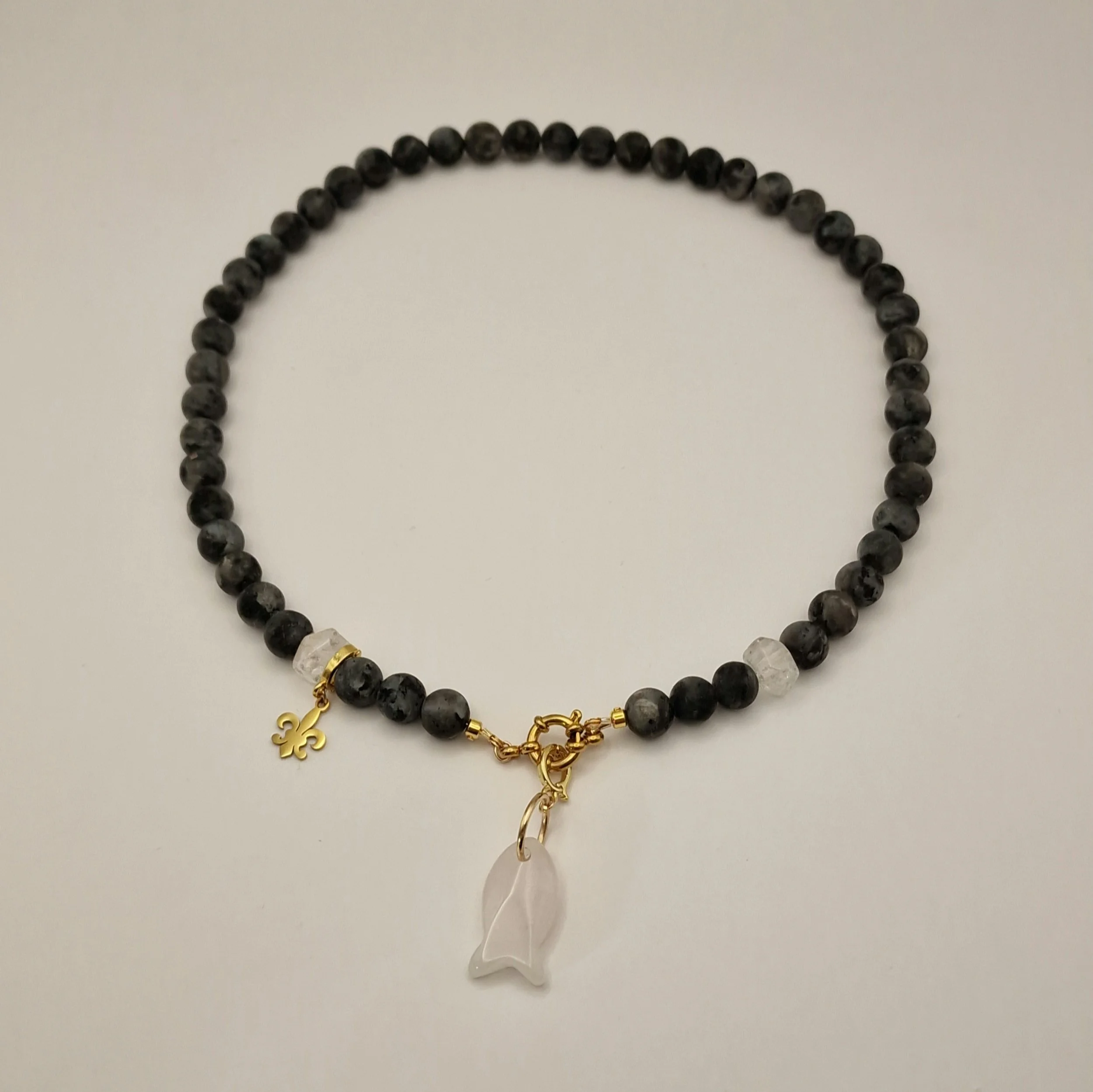 Kette aus schwarzen Spektroliit Perlen kombiniert mit Bergkristall und einem Fischanhänger aus feinem Rosenquarz auf hellem Untergrund