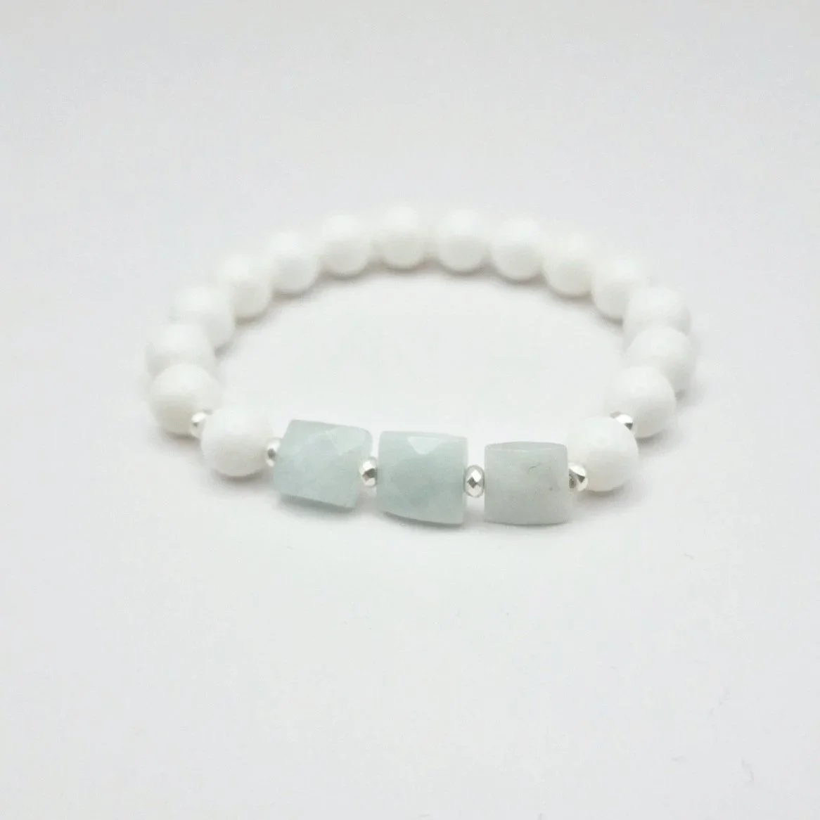 Armband aus weißen Koralleperlen mit versilberten Hämatit Spacern und eisblauen facettierten Rechtecken aus Aquamarin auf hellem Untergrund
