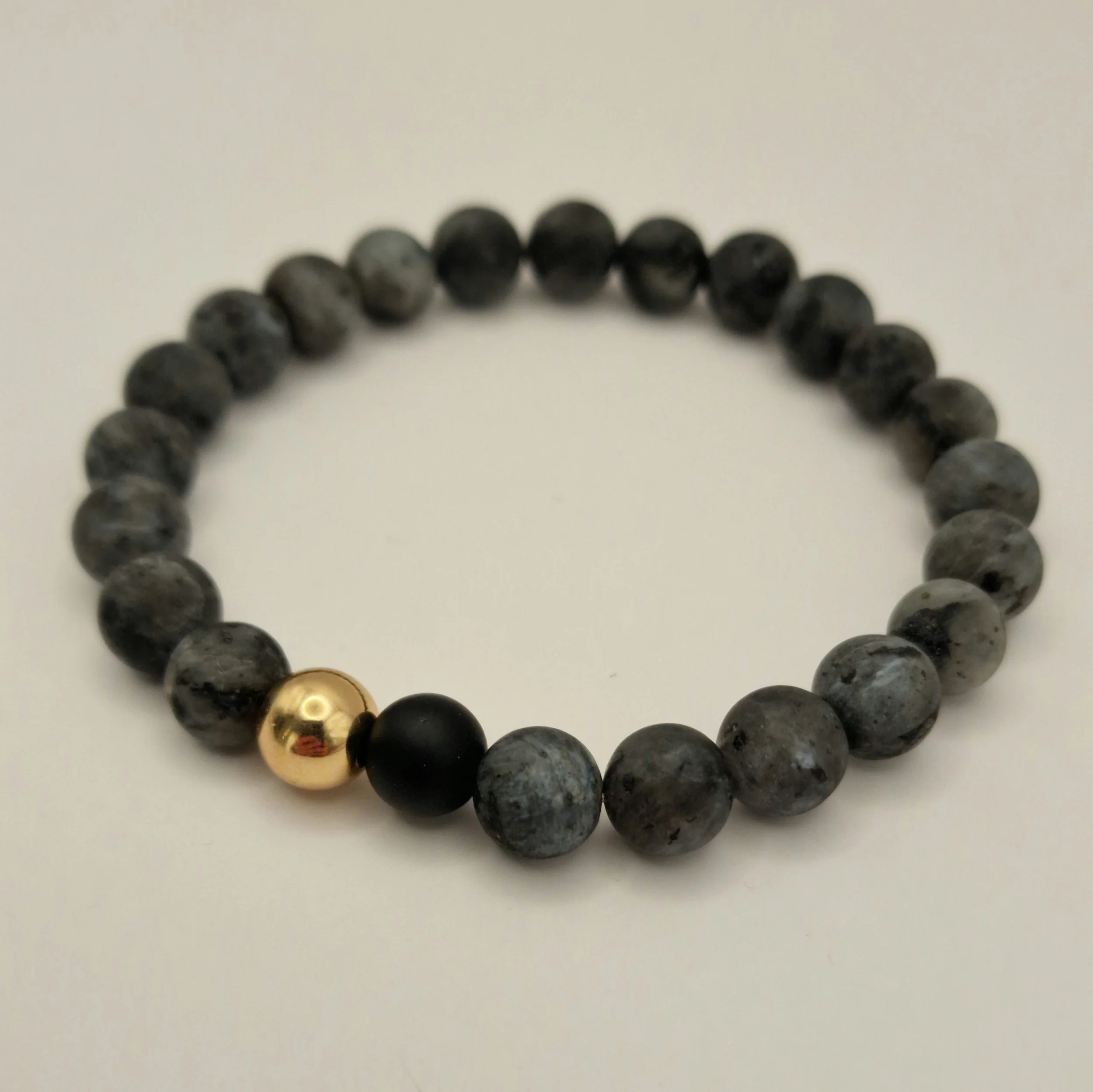 Armband aus schwarzem mattem Labradorit und mattem Obsidian und vergoldetem Hämatit auf weißer Oberfläche liegend