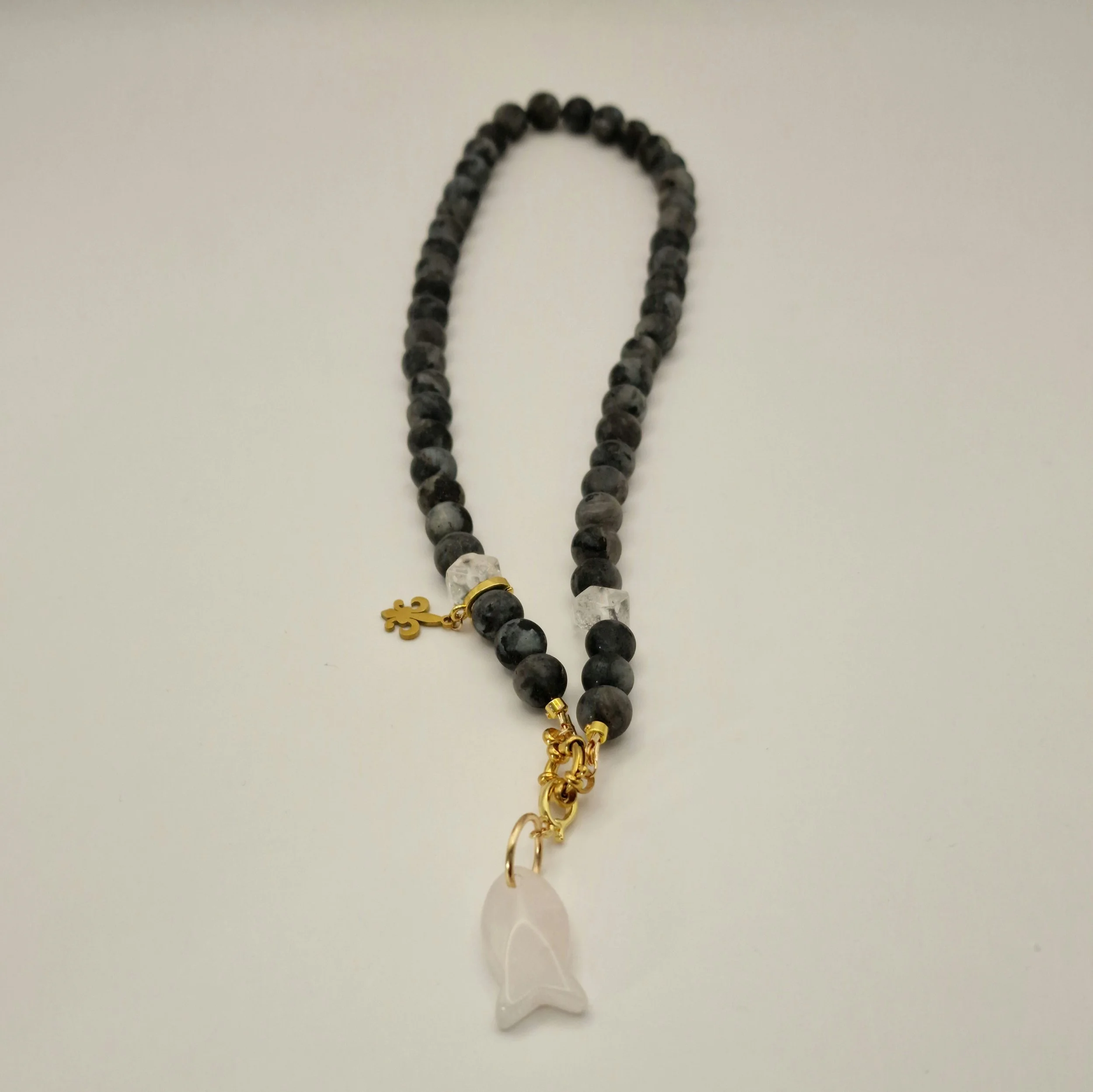 Kette aus schwarzen Spektroliit Perlen kombiniert mit Bergkristall und einem Fischanhänger aus feinem Rosenquarz auf hellem Untergrund