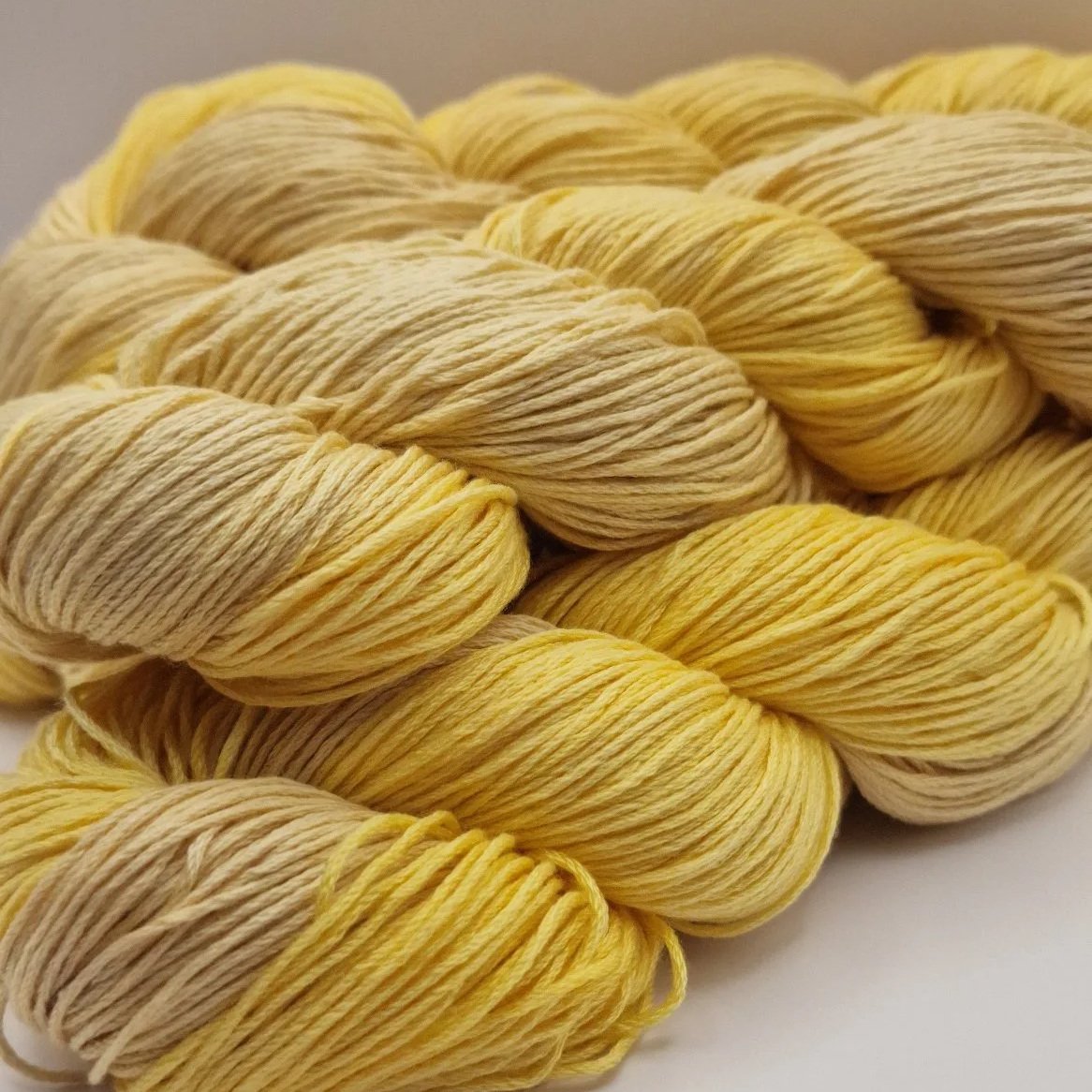 Handgefärbtes Lyocell Garn im Farbverlauf von einem weichen Sandbeige zu einem warmen Gelb auf hellem Untergrund