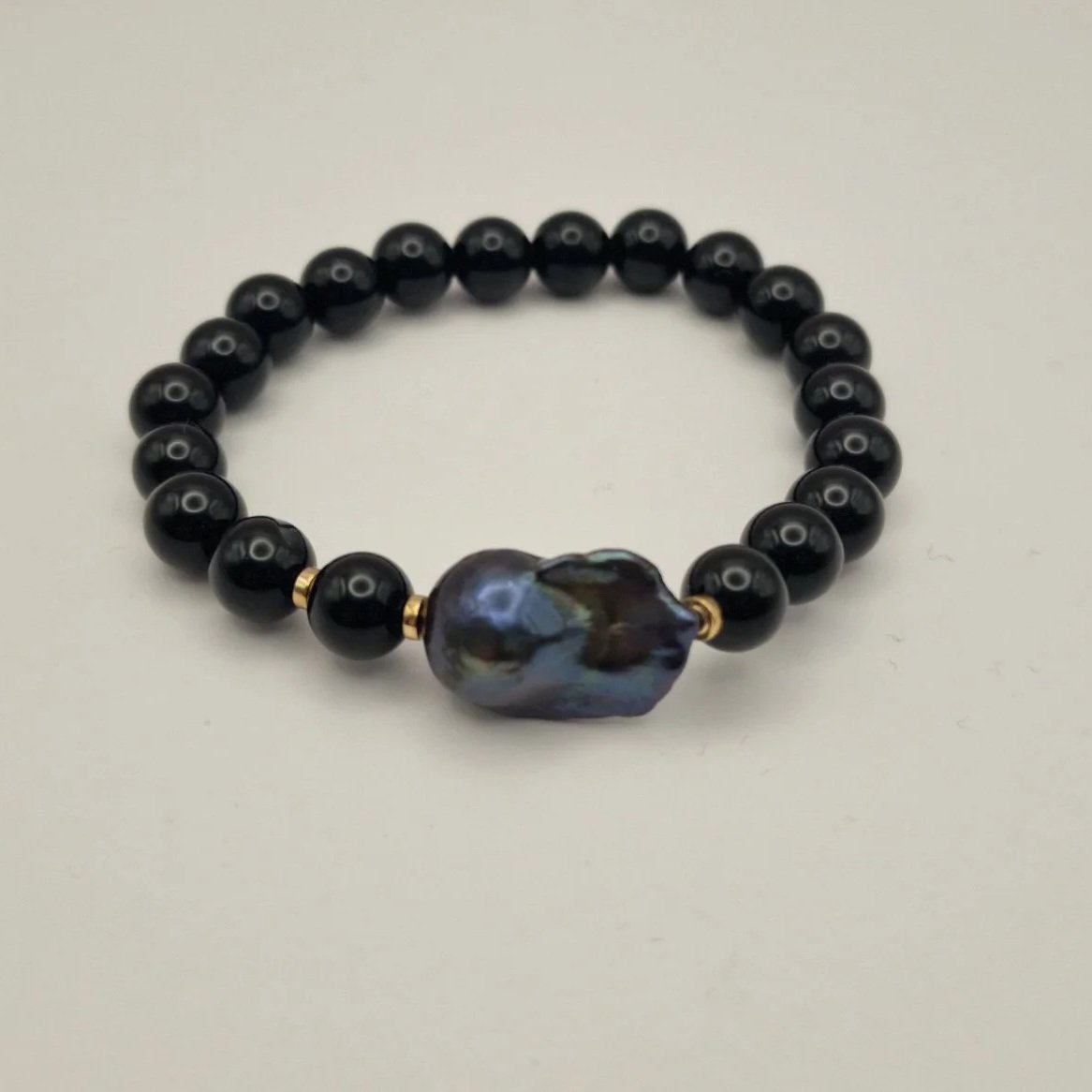 Armband aus Perlen von schwarzem Onyx, vergoldete Hämatitspacer und schwarzer Barockperle auf hellem Untergrund