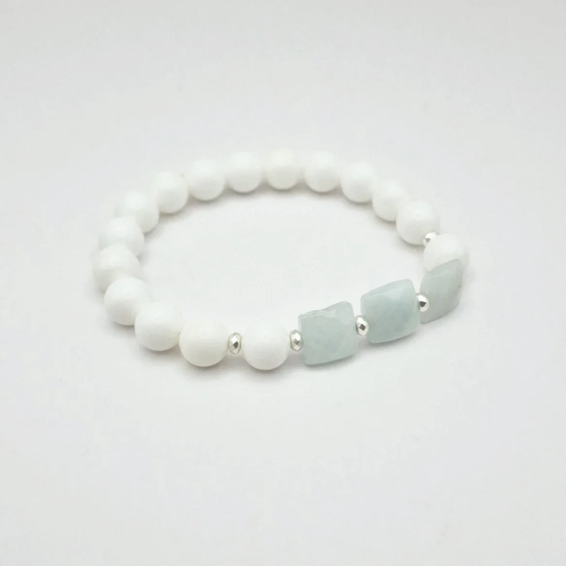 Armband aus weißen Koralleperlen mit versilberten Hämatit Spacern und eisblauen facettierten Rechtecken aus Aquamarin auf hellem Untergrund