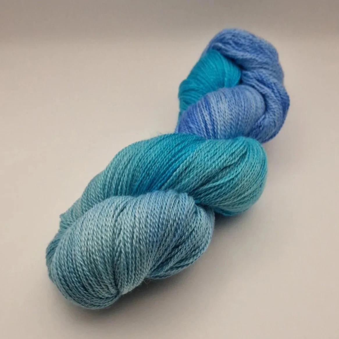 handgefärbte Stränge Wolle aus Schurwolle, Alpaka und Seide in blau, türkis und hellgrün auf weißem Untergrund das an Tropische Gewässer erinnert