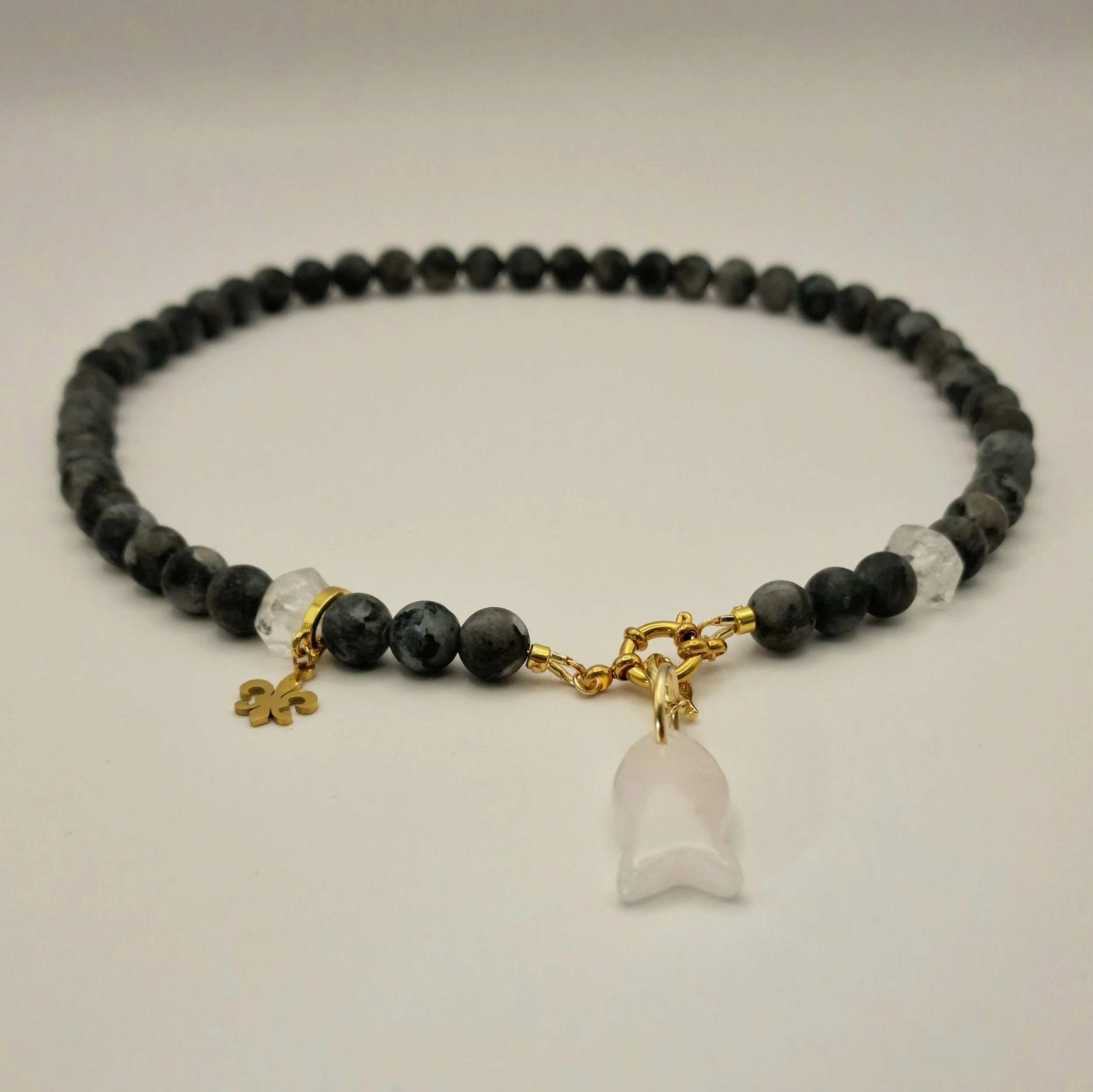 Kette aus schwarzen Spektroliit Perlen kombiniert mit Bergkristall und einem Fischanhänger aus feinem Rosenquarz auf hellem Untergrund