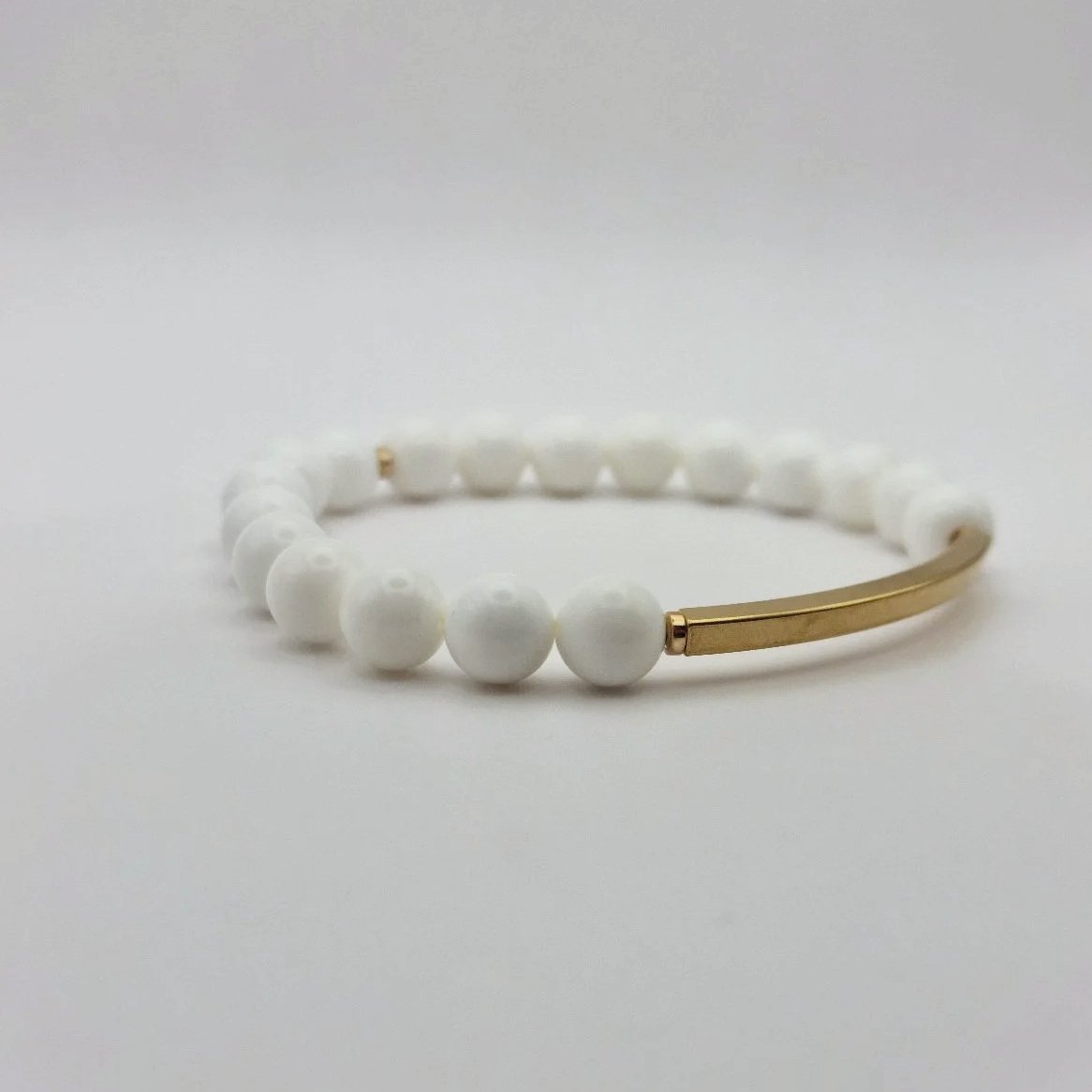 Puristisches weißes Armband Hebe Ambrosia aus echten Korallenperlen mit einem geschwungenen, vergoldeten Edelstahl-Röhrchen.