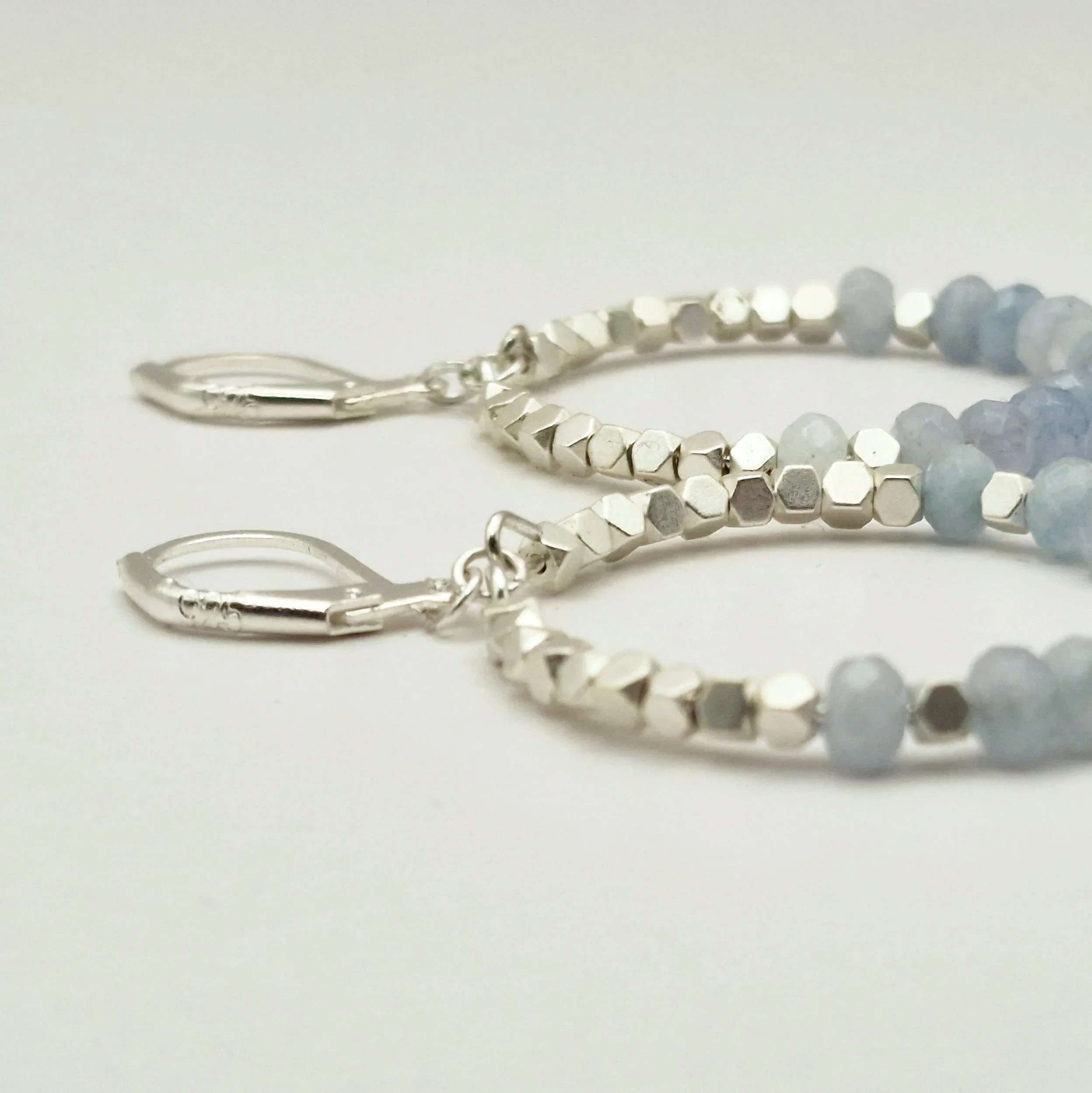 runde Hoop - Ohrringe in Silber mit weißvergoldetem Hämatit Perlen und facettierten Aquamarinperlen auf hellem Untergrund