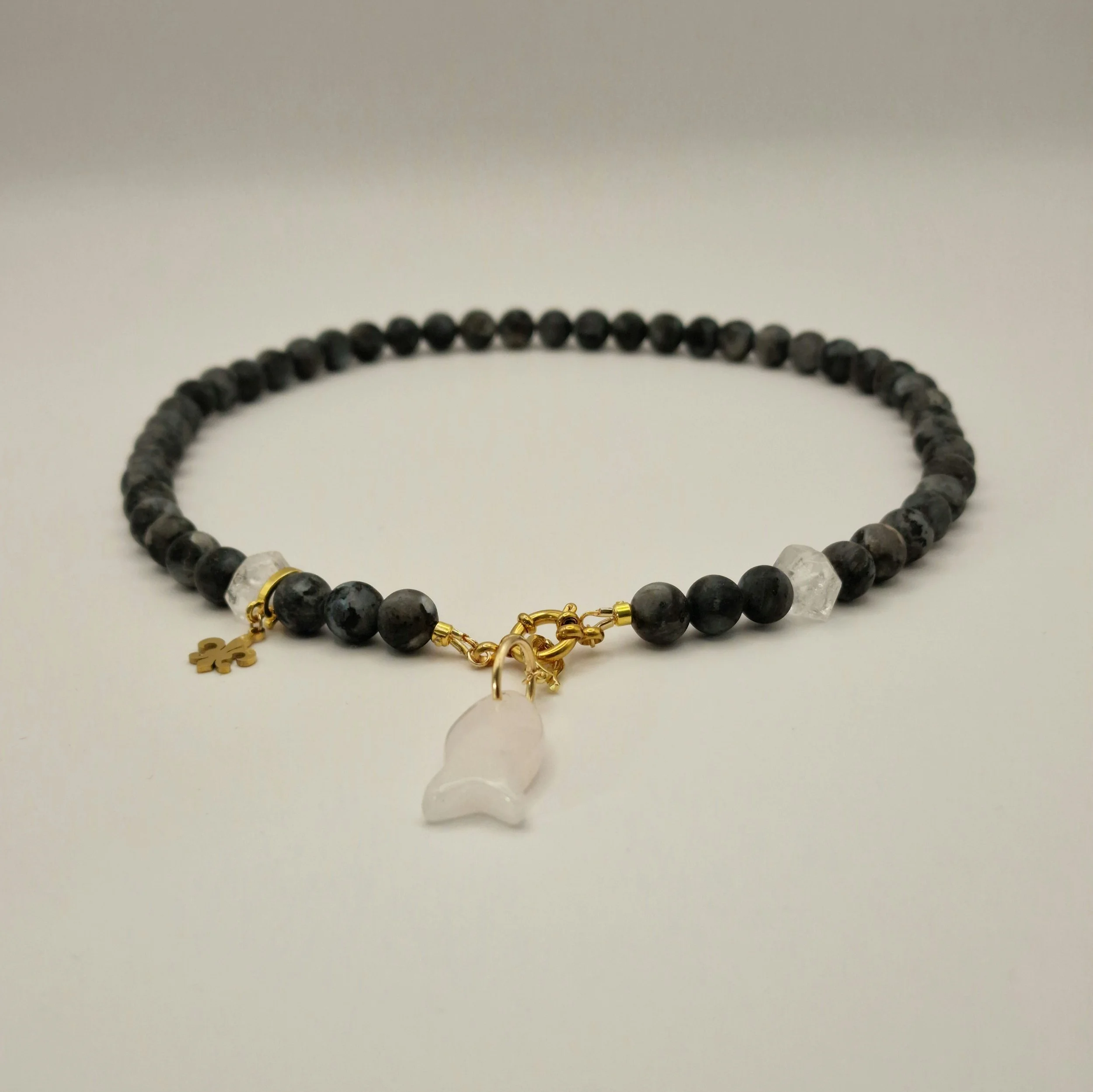 Kette aus schwarzen Spektroliit Perlen kombiniert mit Bergkristall und einem Fischanhänger aus feinem Rosenquarz auf hellem Untergrund