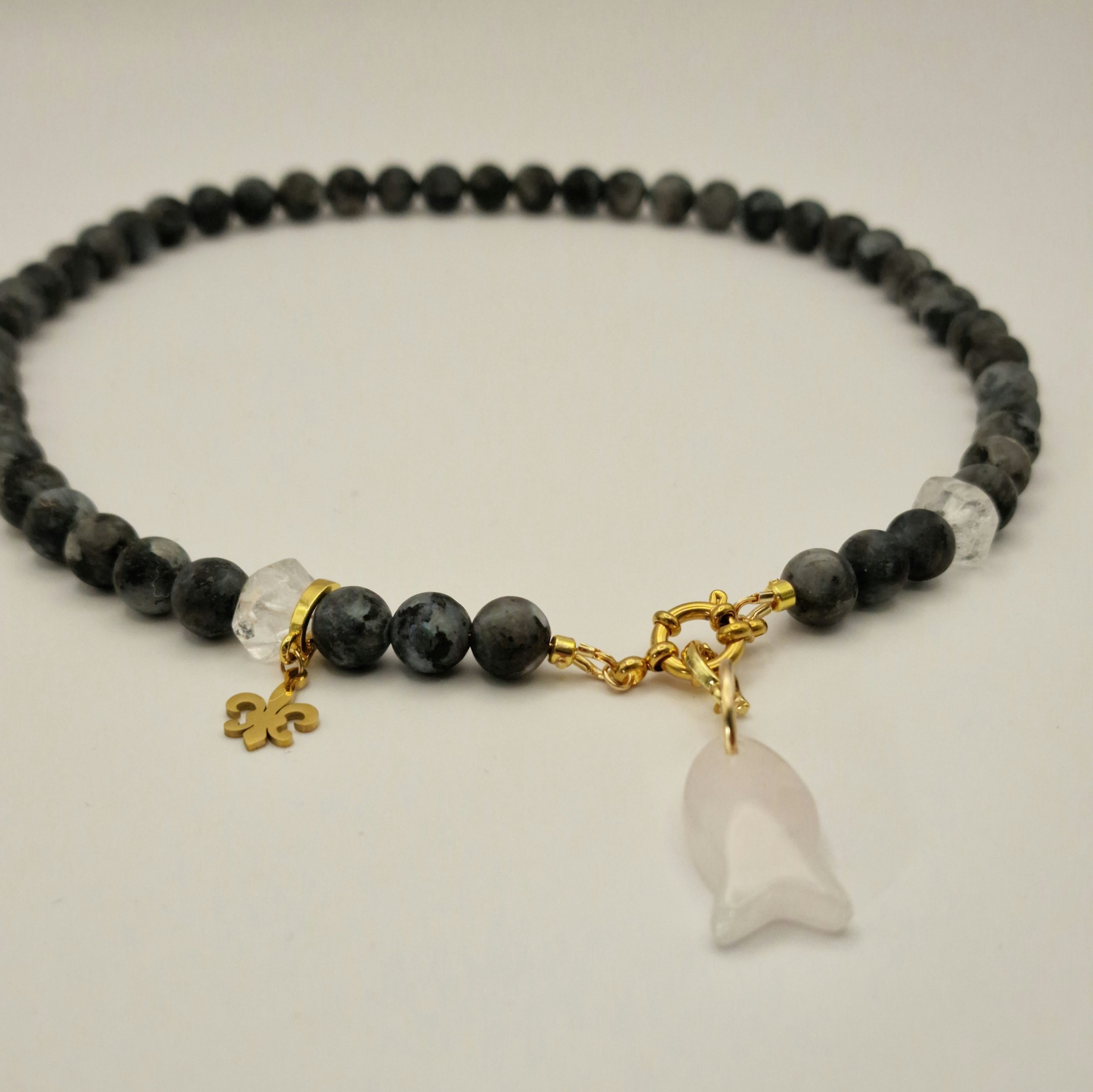 Kette aus schwarzen Spektroliit Perlen kombiniert mit Bergkristall und einem Fischanhänger aus feinem Rosenquarz auf hellem Untergrund