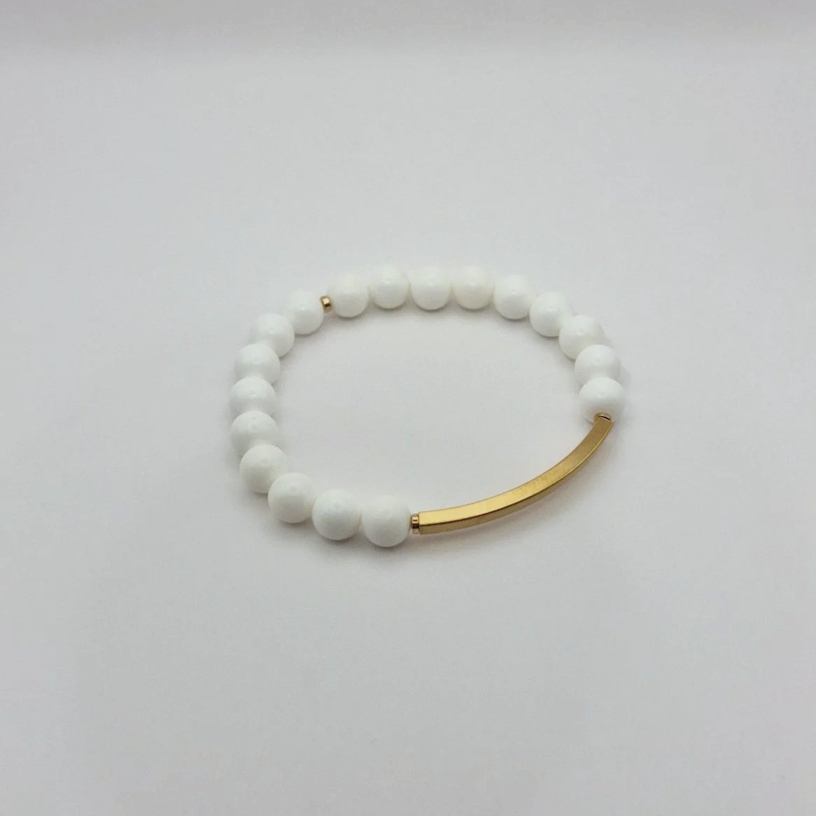 Puristisches weißes Armband Hebe Ambrosia aus echten Korallenperlen mit einem geschwungenen, vergoldeten Edelstahl-Röhrchen.
