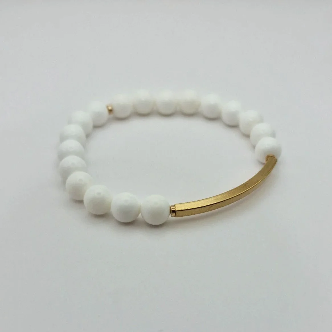Puristisches weißes Armband Hebe Ambrosia aus echten Korallenperlen mit einem geschwungenen, vergoldeten Edelstahl-Röhrchen.