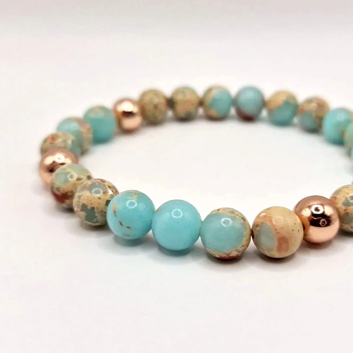 Armband aus rosévergoldeten, hellblauen und hellbraunen Perlen auf weißem Untergrund