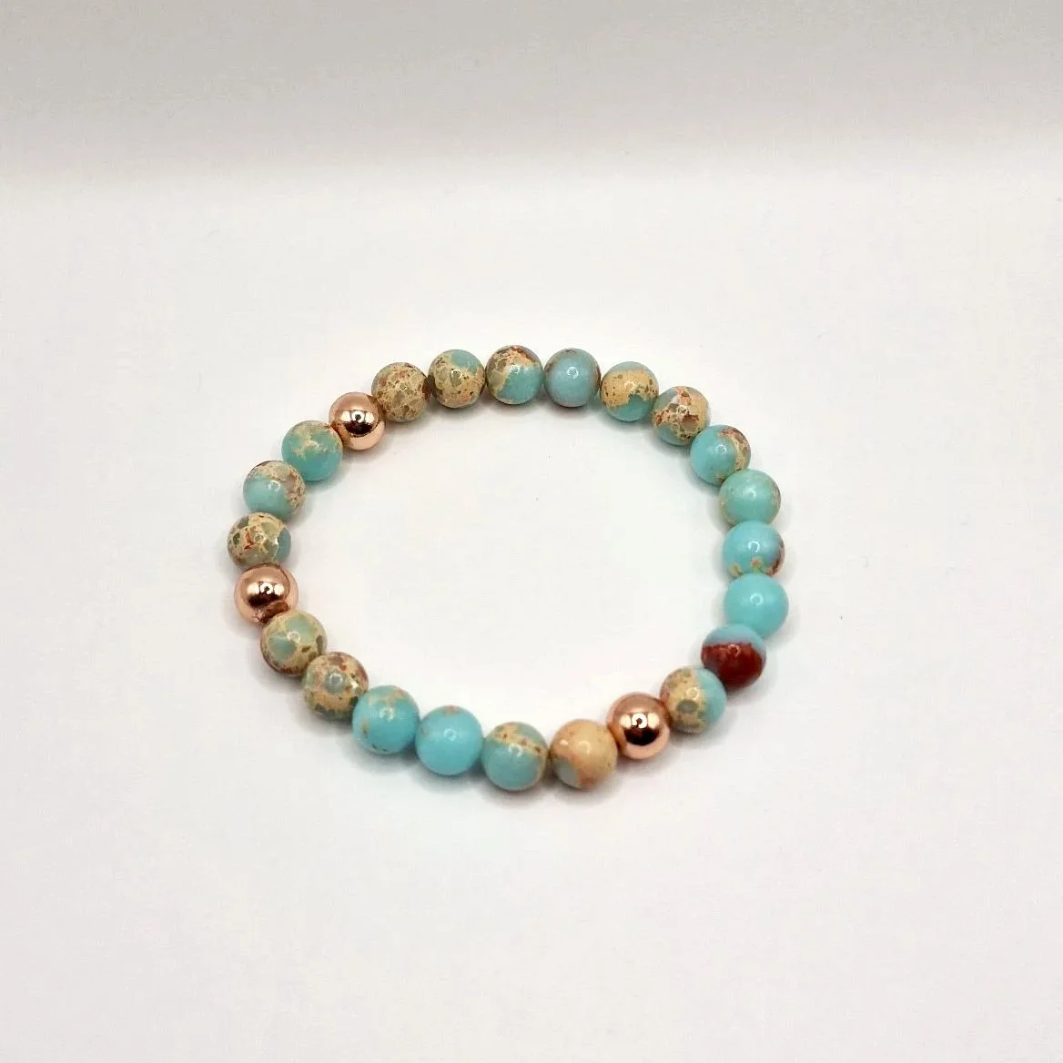 Armband aus rosévergoldeten, hellblauen und hellbraunen Perlen auf weißem Untergrund