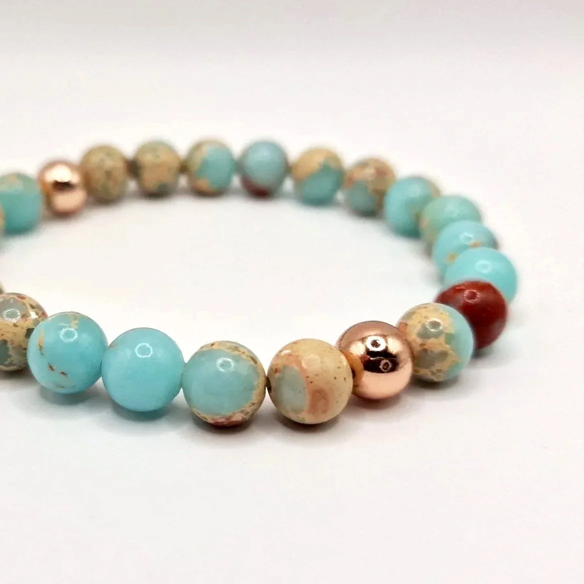 Armband aus rosévergoldeten, hellblauen und hellbraunen Perlen auf weißem Untergrund