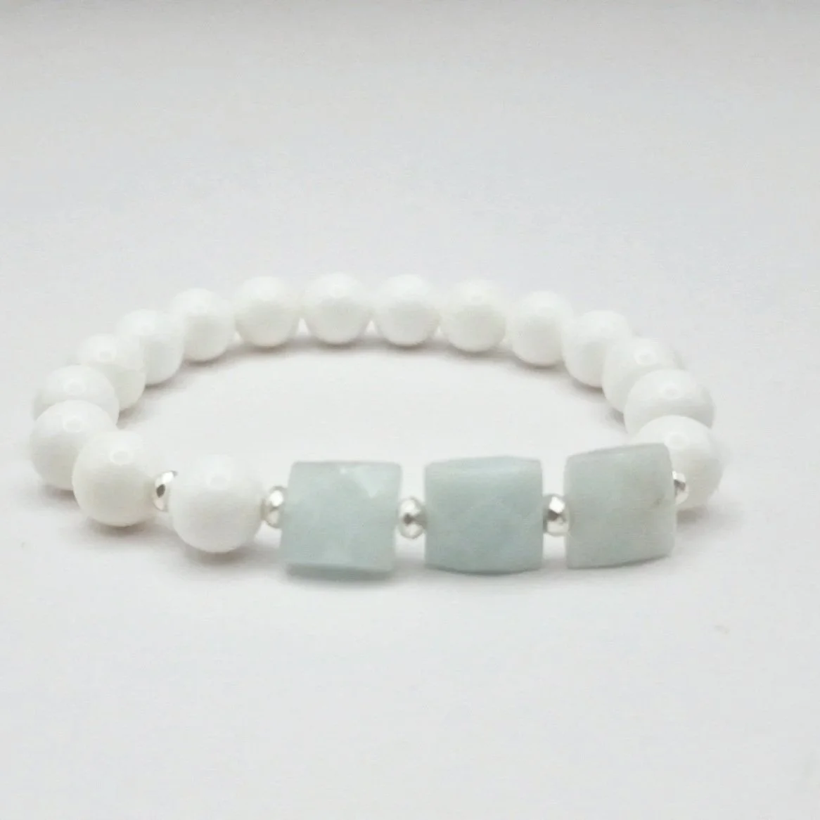 Armband aus weißen Koralleperlen mit versilberten Hämatit Spacern und eisblauen facettierten Rechtecken aus Aquamarin auf hellem Untergrund