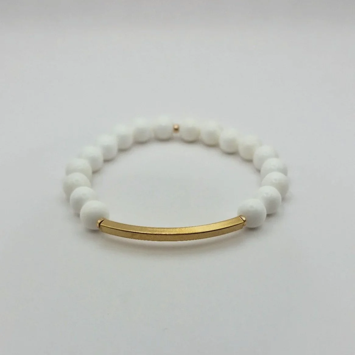 Puristisches weißes Armband Hebe Ambrosia aus echten Korallenperlen mit einem geschwungenen, vergoldeten Edelstahl-Röhrchen.