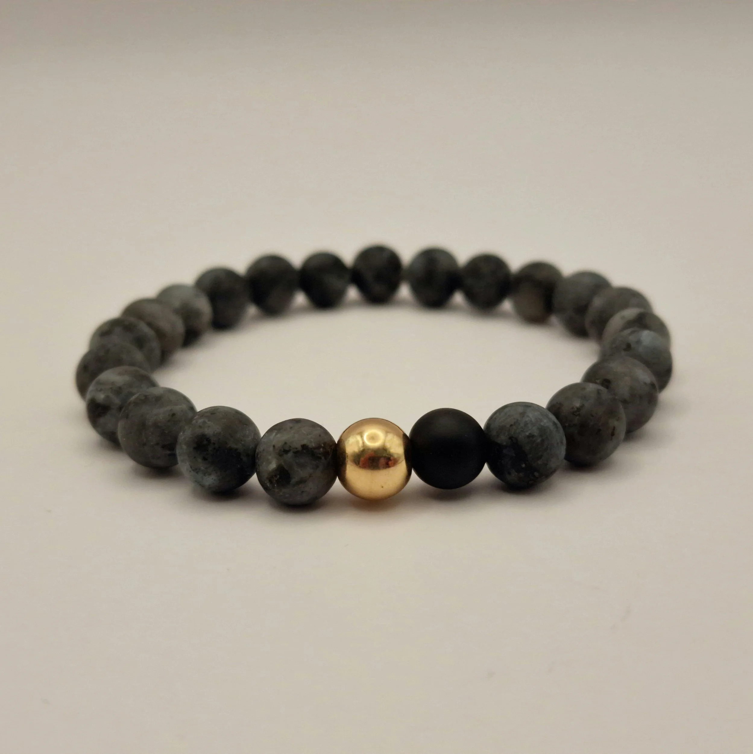 Armband aus schwarzem mattem Labradorit und mattem Obsidian und vergoldetem Hämatit auf weißer Oberfläche liegend