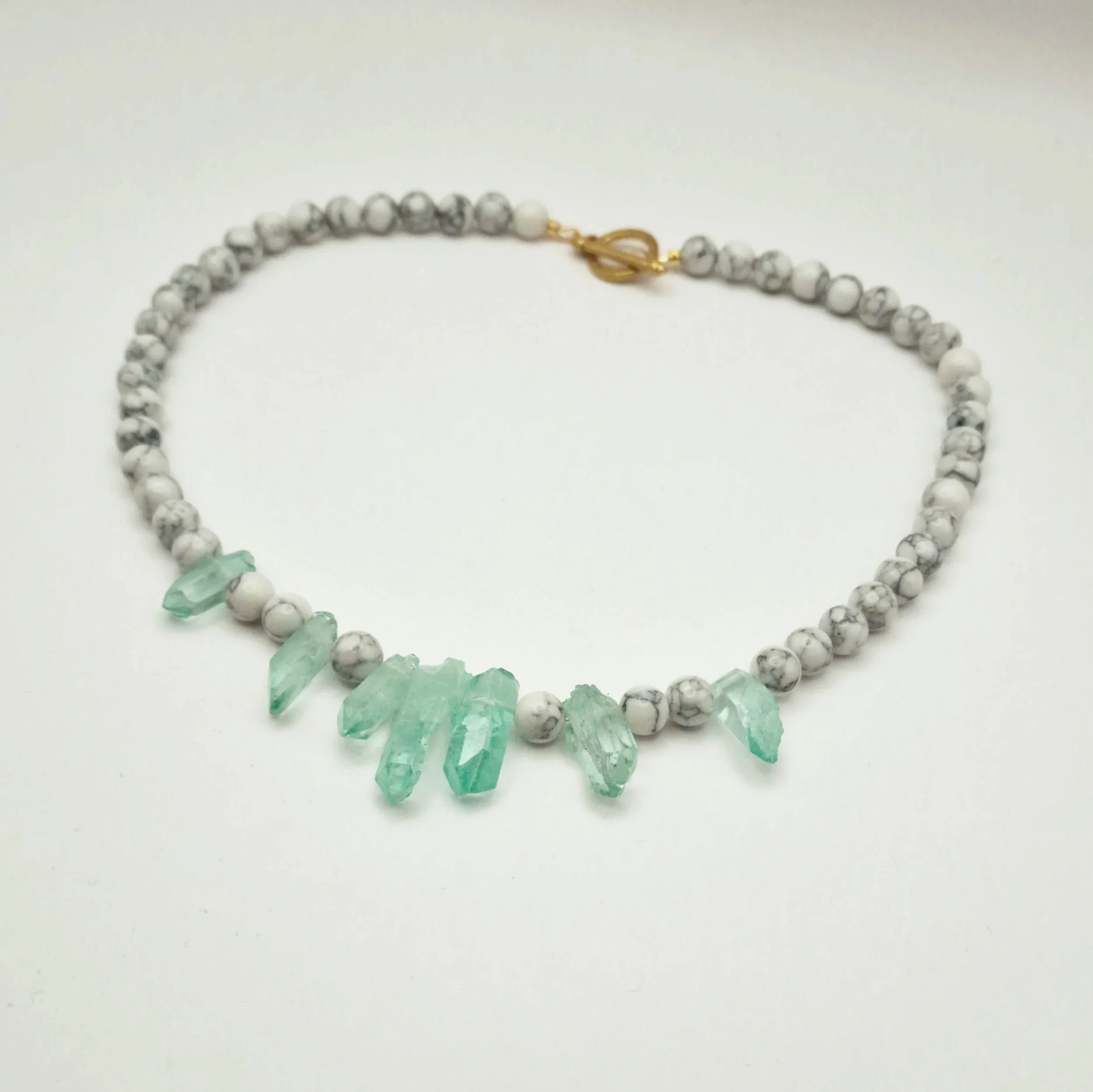 Kette aus weißen Howlith Perlen mit grün gefärbten Kristallspitzen und vergoldetem Verschluss  auf hellem Untergrund