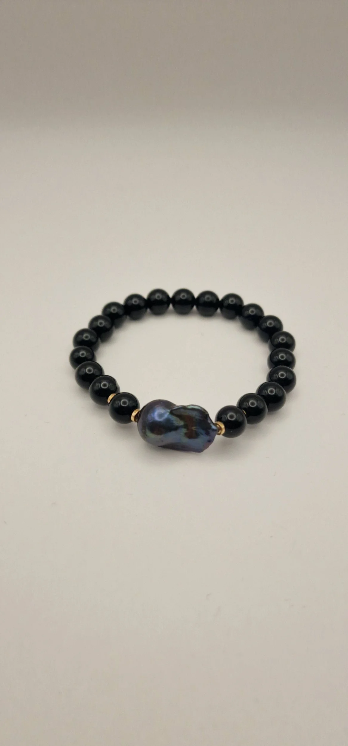 Armband aus Perlen von schwarzem Onyx, vergoldete Hämatitspacer und schwarzer Barockperle auf hellem Untergrund