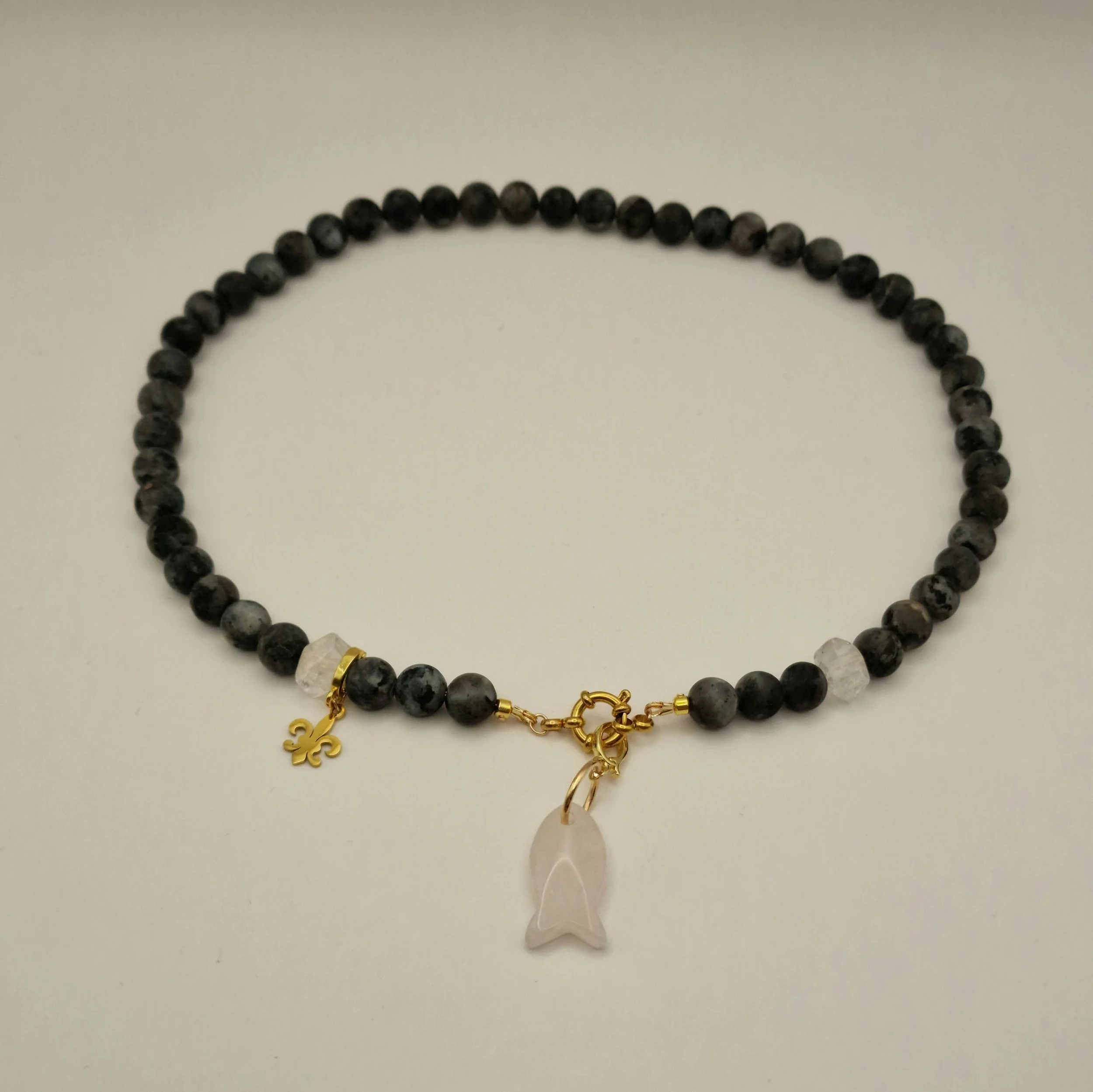 Kette aus schwarzen Spektroliit Perlen kombiniert mit Bergkristall und einem Fischanhänger aus feinem Rosenquarz auf hellem Untergrund