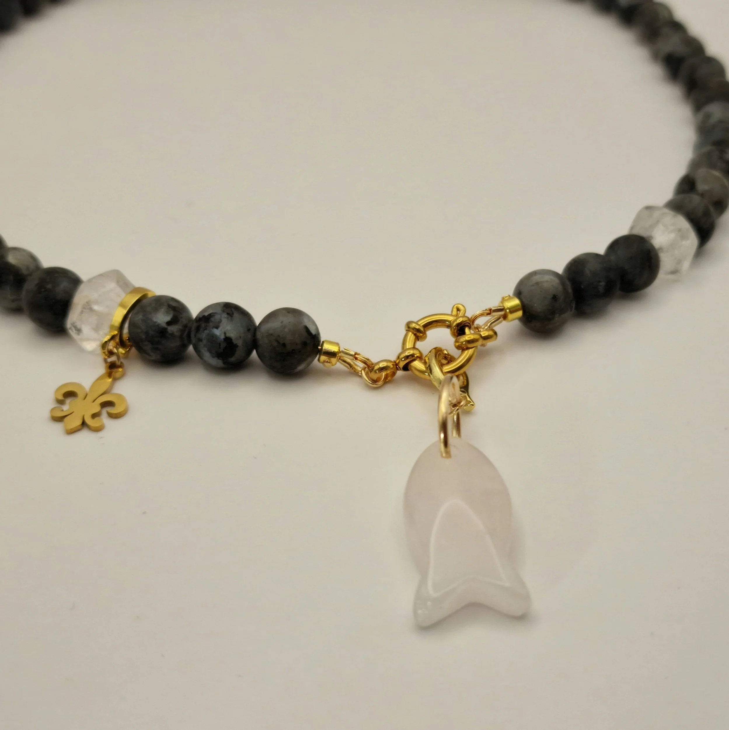 Kette aus schwarzen Spektroliit Perlen kombiniert mit Bergkristall und einem Fischanhänger aus feinem Rosenquarz auf hellem Untergrund