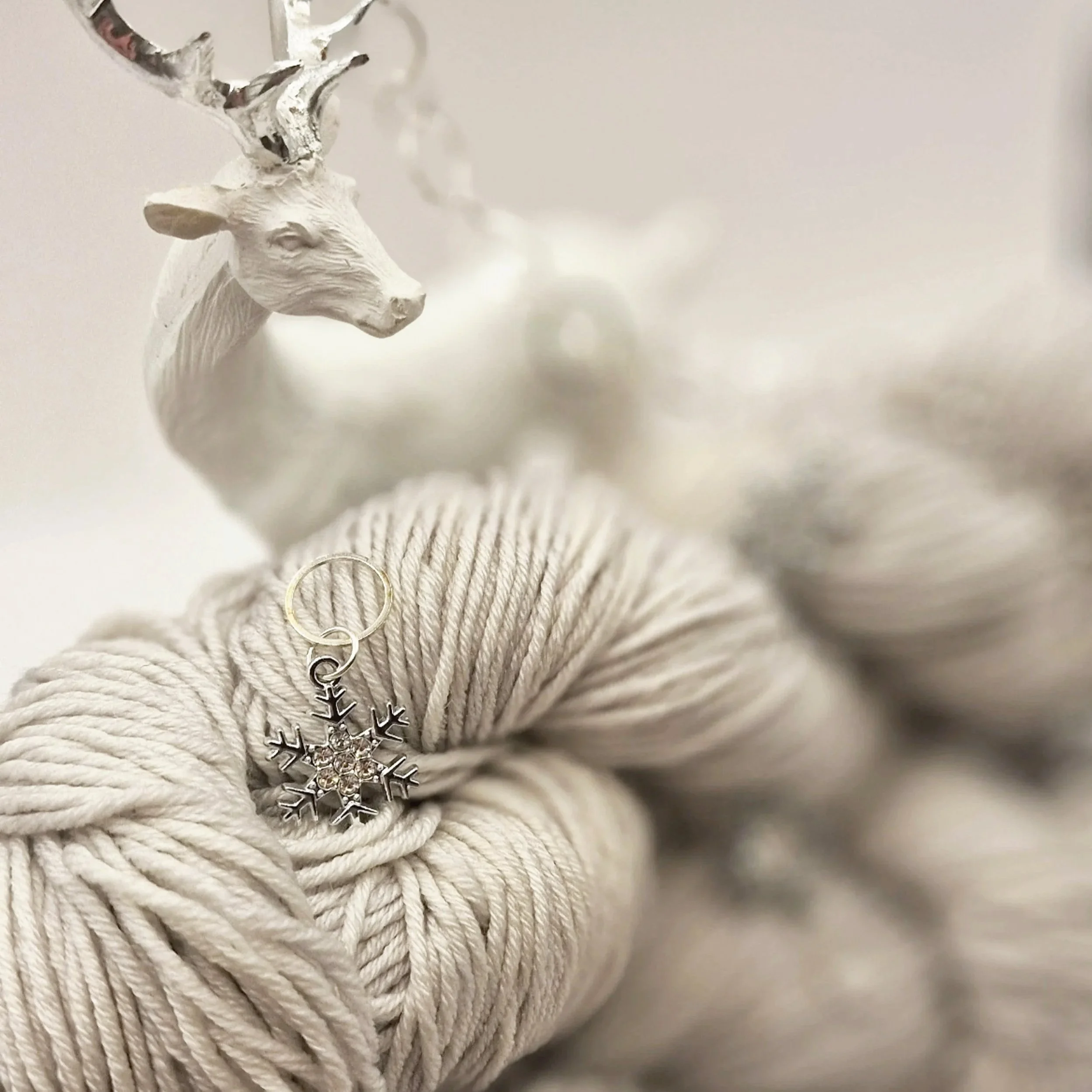 Silbergraues Merino Seidengarn mit einem Maschenmarkierer in silberfarbener Schneeflockenform und einer Hirschdekoration