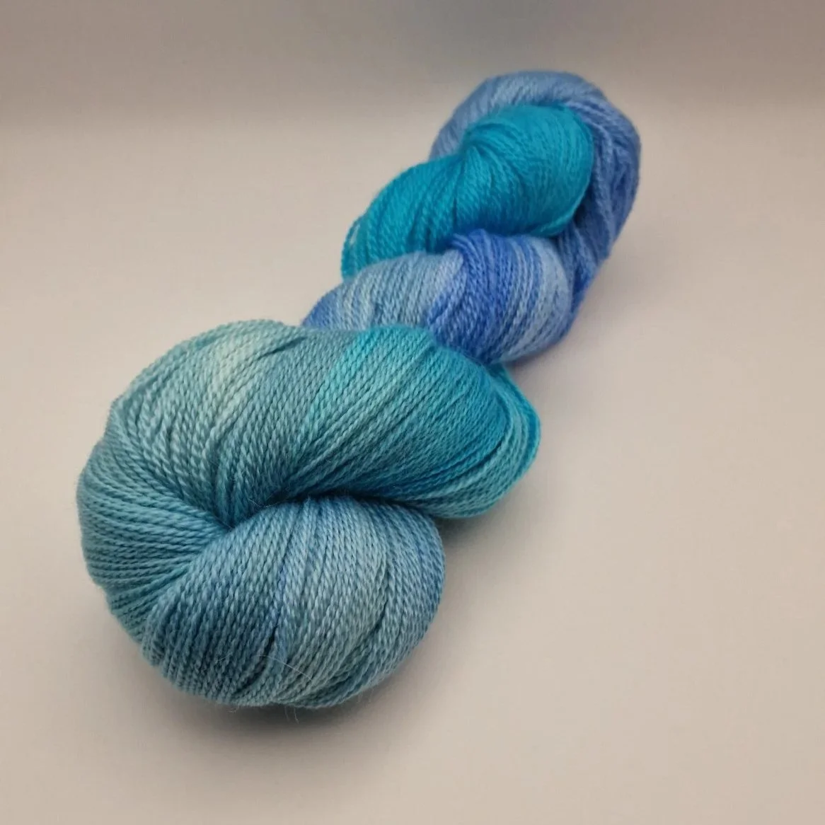 handgefärbte Stränge Wolle aus Schurwolle, Alpaka und Seide in blau, türkis und hellgrün auf weißem Untergrund das an Tropische Gewässer erinnert