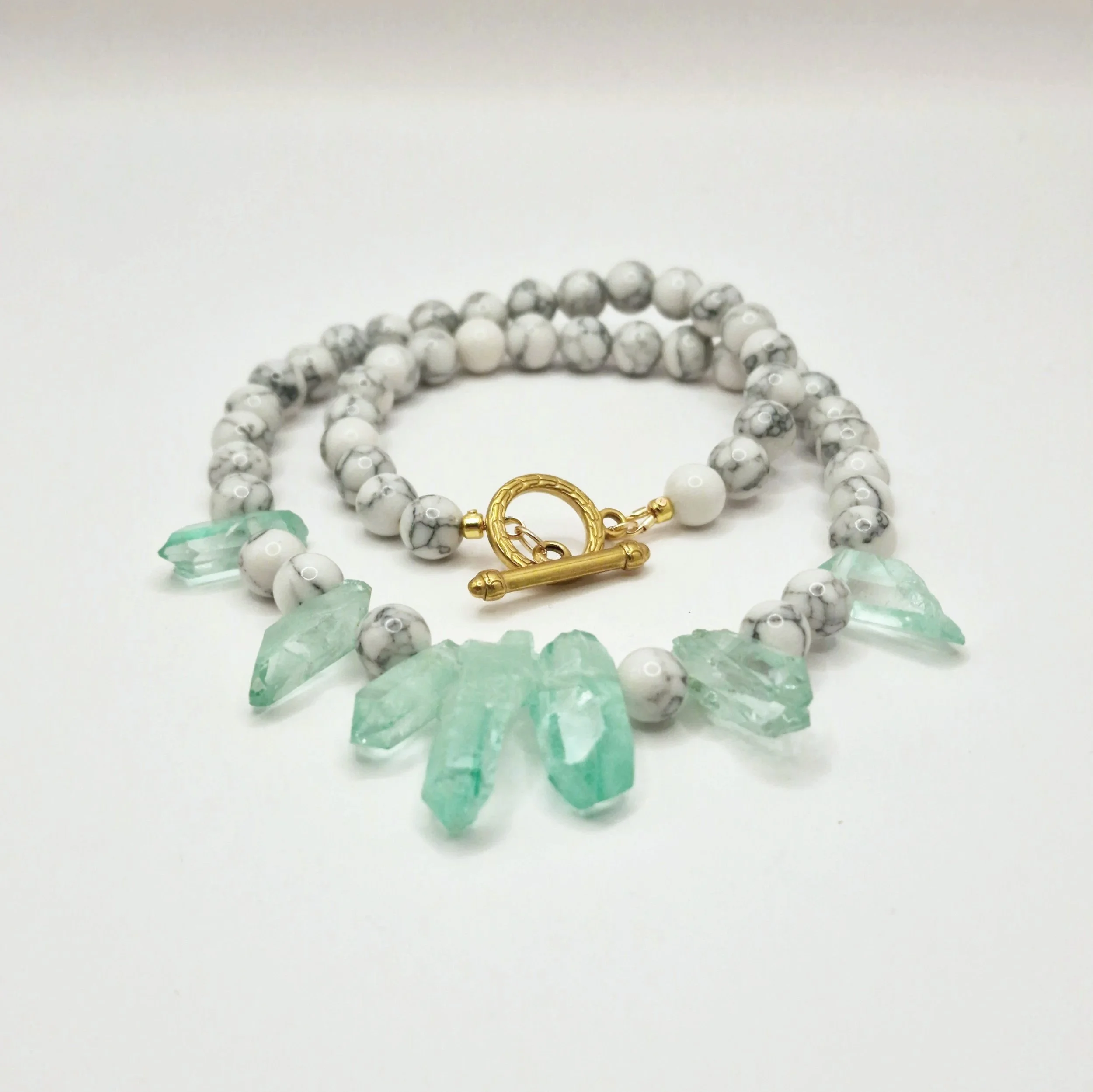 Kette aus weißen Howlith Perlen mit grün gefärbten Kristallspitzen und vergoldetem Verschluss  auf hellem Untergrund