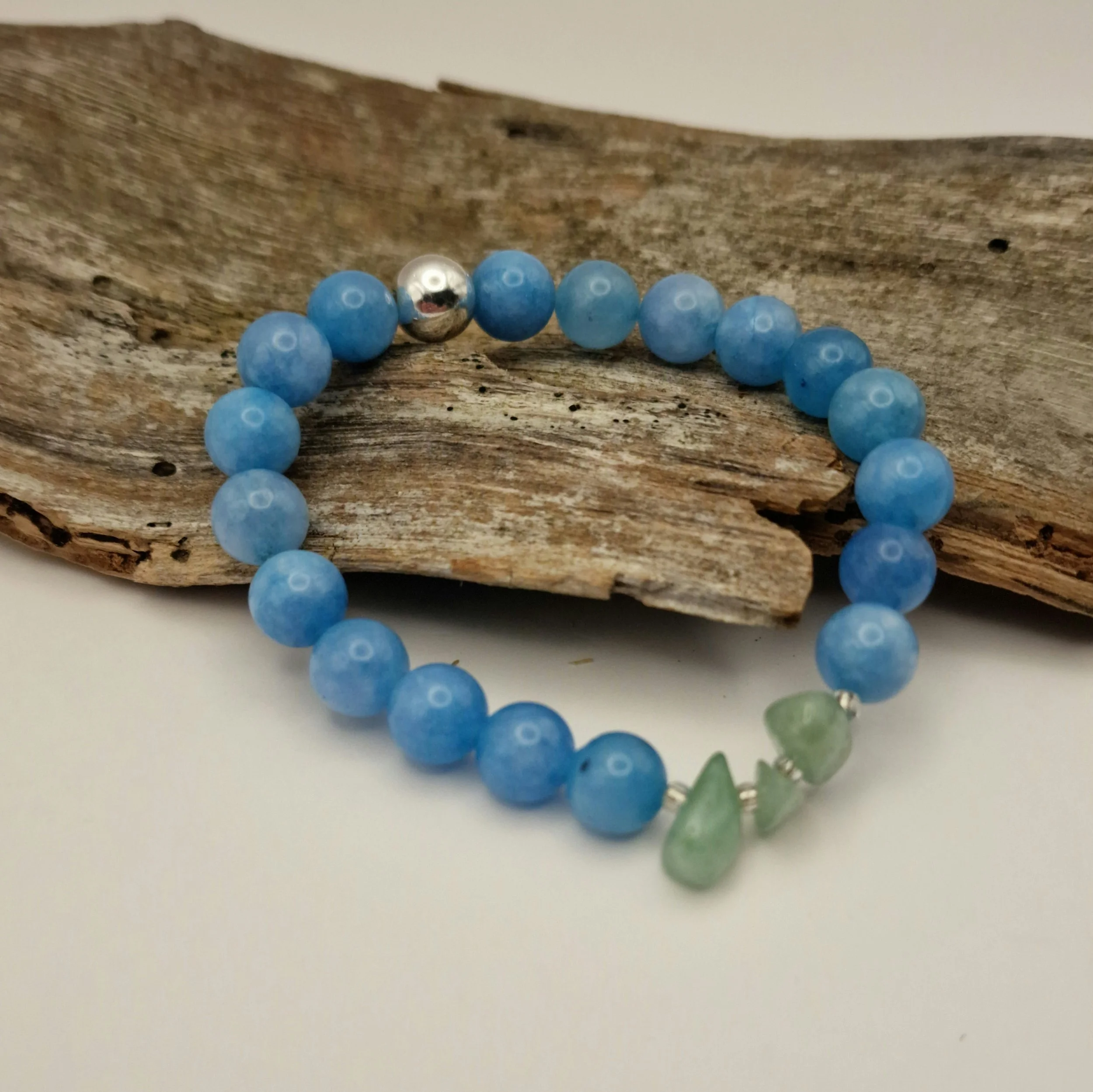 Armband aus blauen Aquamarinperlen mit Amazonitsplittern und einer versilberten Hämatit-Perle auf Treibholz und hellem Untergrund