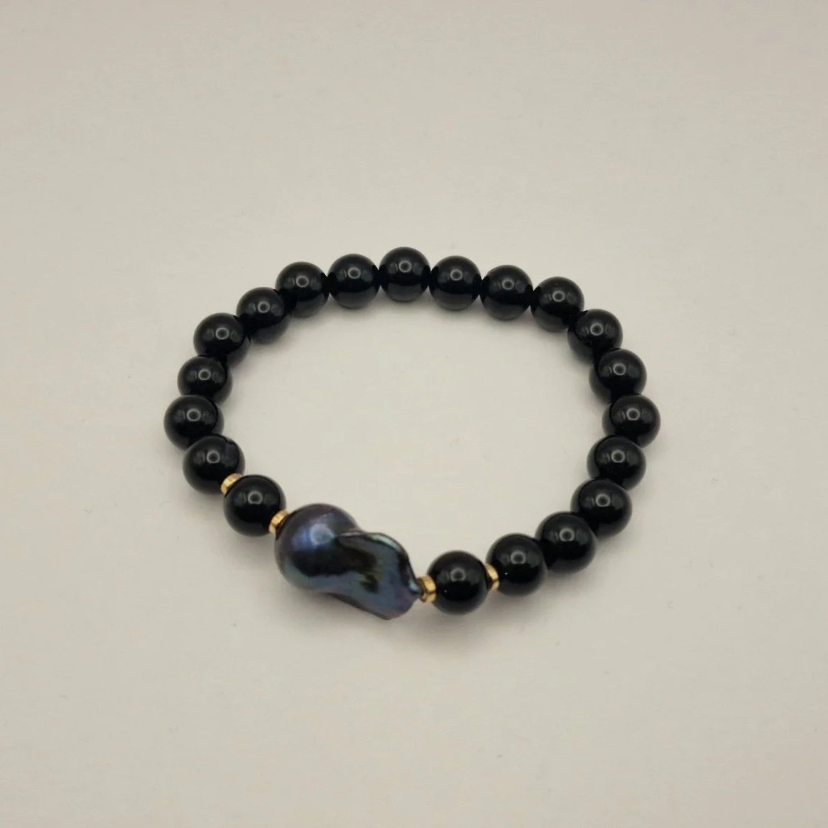 Armband aus Perlen von schwarzem Onyx, vergoldete Hämatitspacer und schwarzer Barockperle auf hellem Untergrund