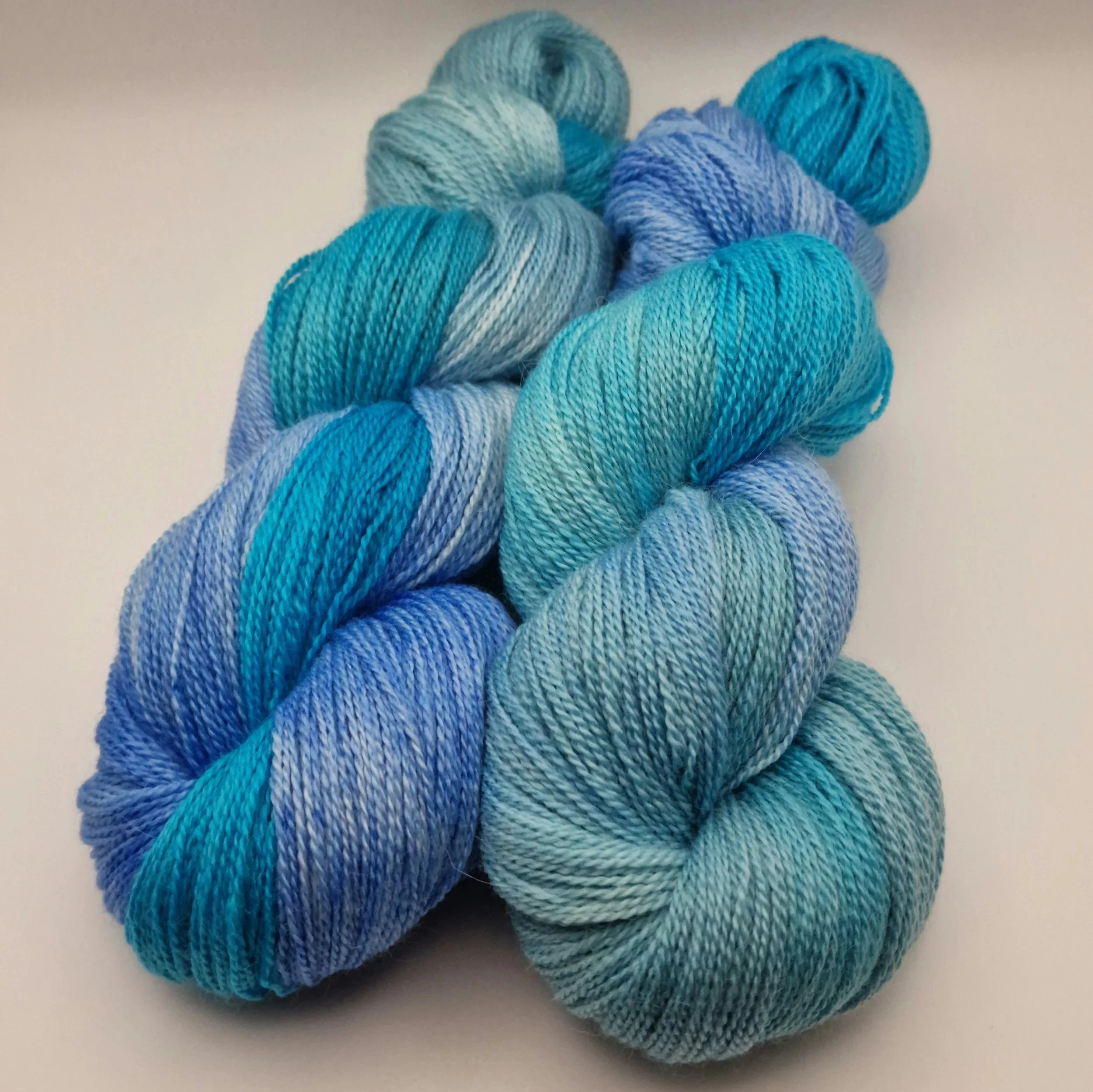 handgefärbte Stränge Wolle aus Schurwolle, Alpaka und Seide in blau, türkis und hellgrün auf weißem Untergrund das an Tropische Gewässer erinnert