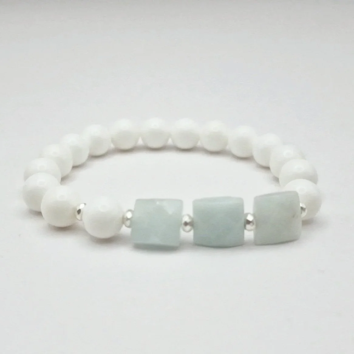 Armband aus weißen Koralleperlen mit versilberten Hämatit Spacern und eisblauen facettierten Rechtecken aus Aquamarin auf hellem Untergrund