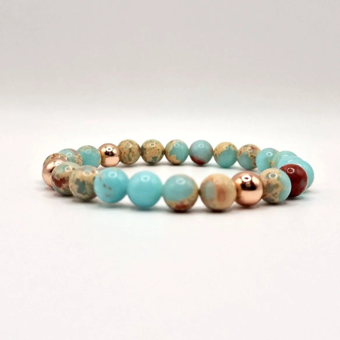 Armband aus rosévergoldeten, hellblauen und hellbraunen Perlen auf weißem Untergrund
