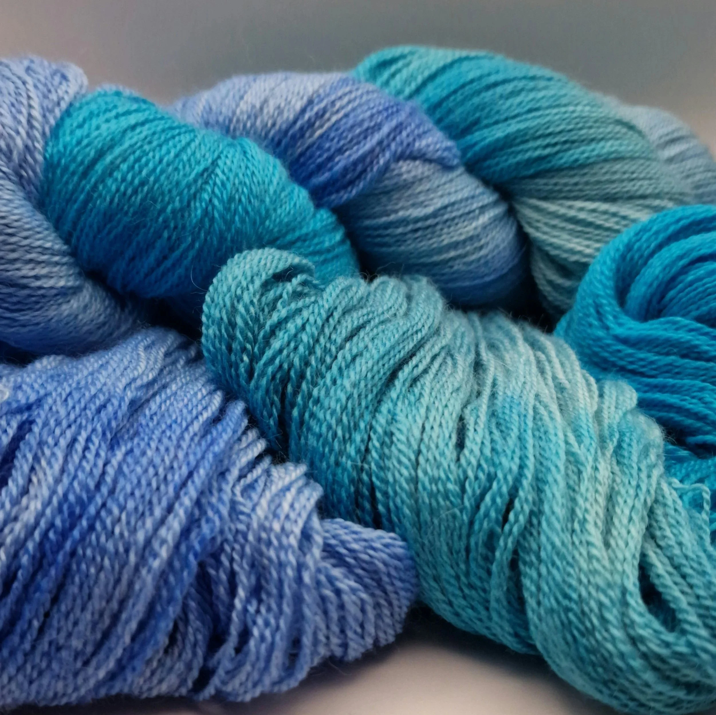 handgefärbte Stränge Wolle aus Schurwolle, Alpaka und Seide in blau, türkis und hellgrün auf weißem Untergrund das an Tropische Gewässer erinnert