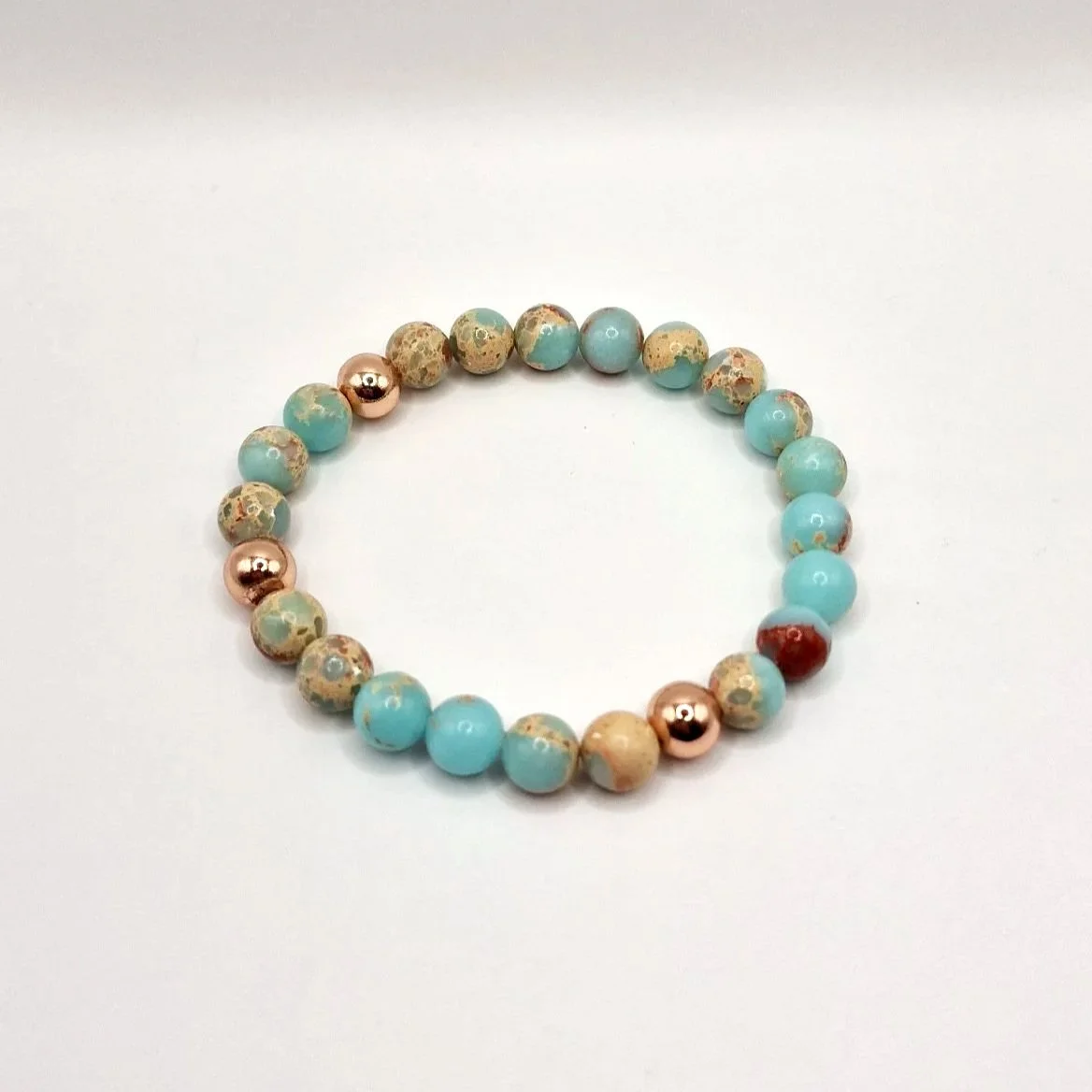 Armband aus rosévergoldeten, hellblauen und hellbraunen Perlen auf weißem Untergrund